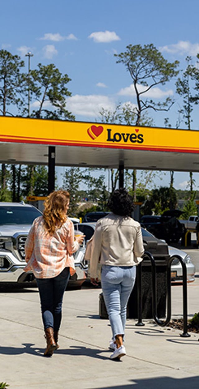 Two people walking toward a Love’s Travel Stop storefront on a sunny day.
