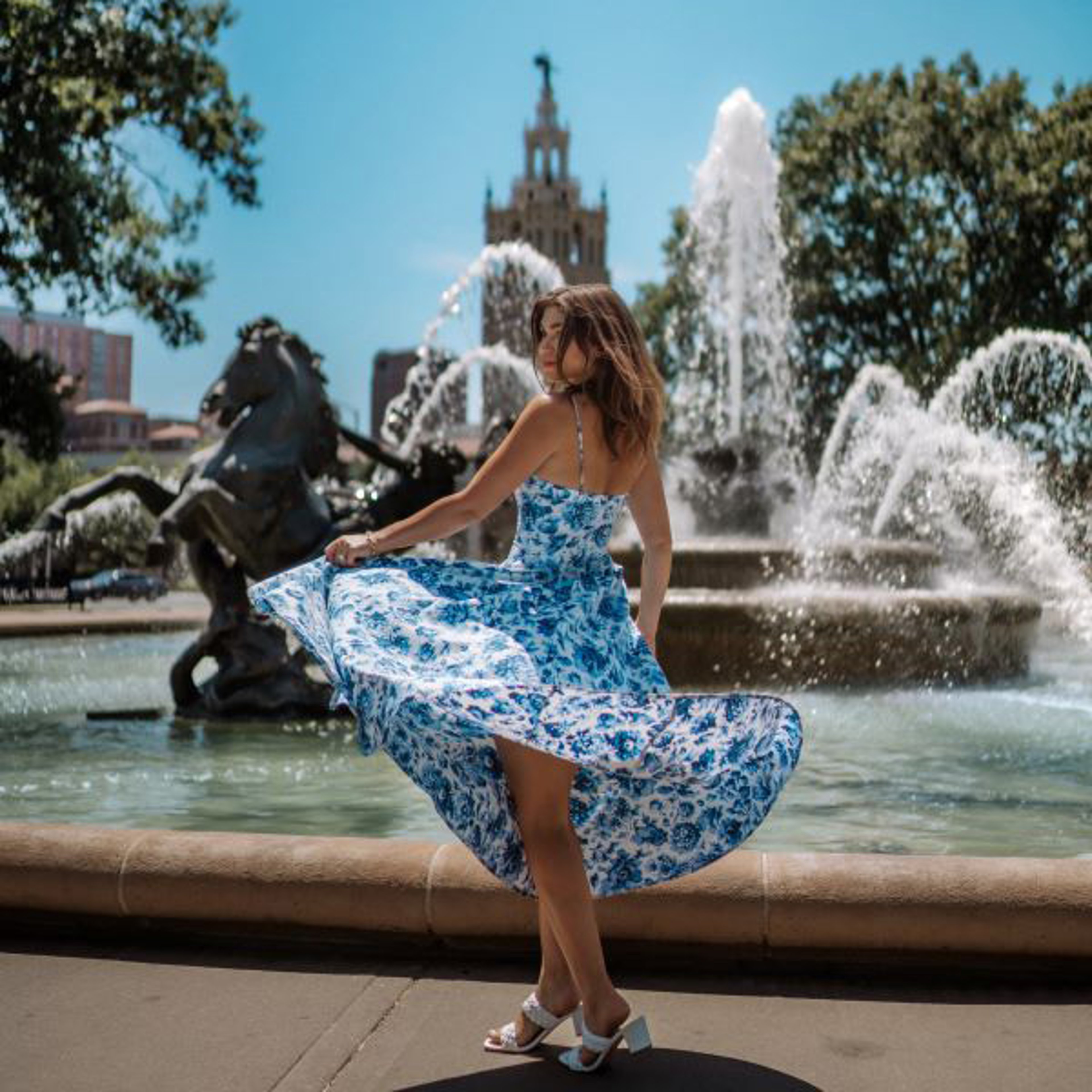 AAA Discounts Marriott Bonvoy Woman twirling in a blue floral dress near a fountain with horse sculptures