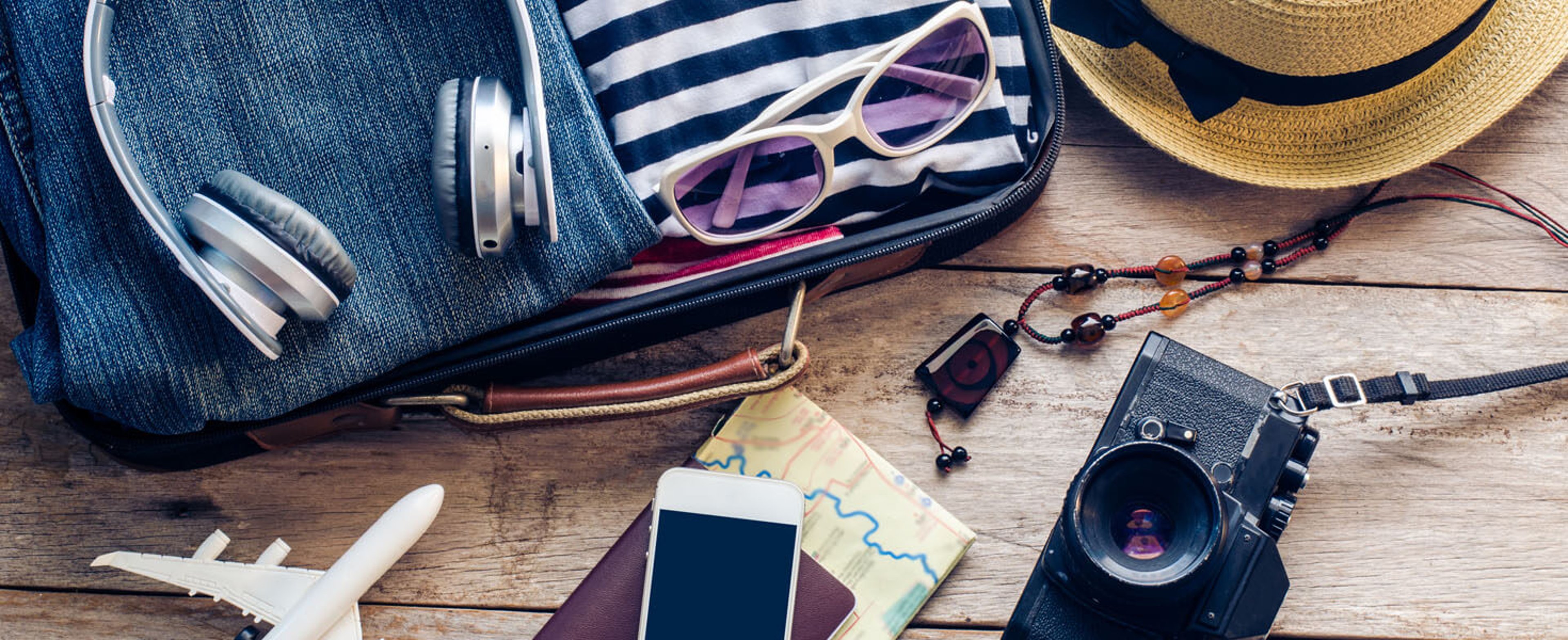 Camera, passport, and luggage with clothes and a hat laying on a table