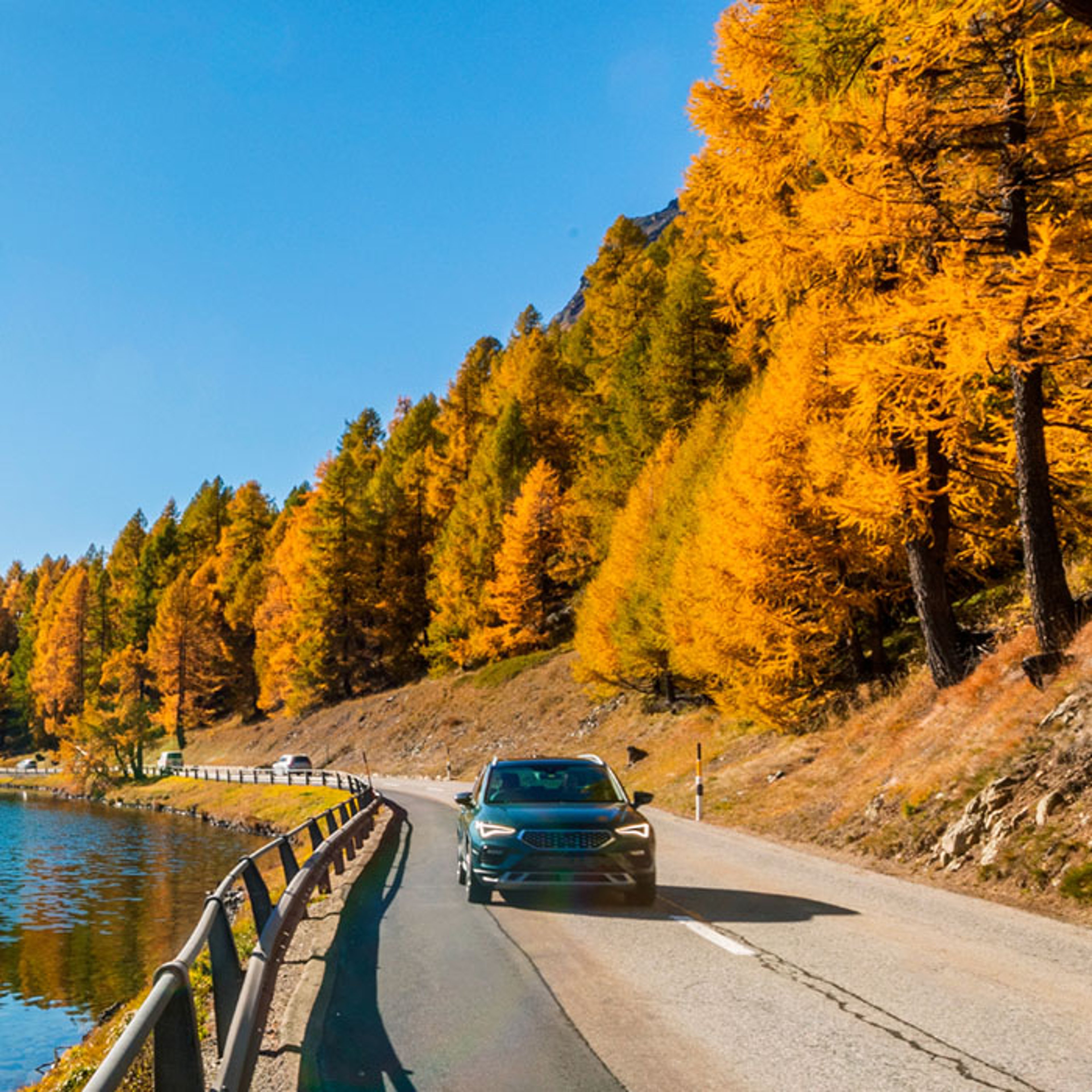 Car driving down highway by lake in autumn