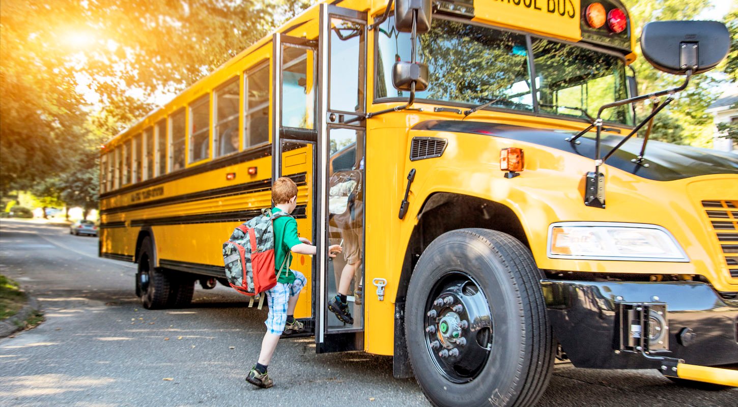 Two young children boarding a school bus on a sunny day