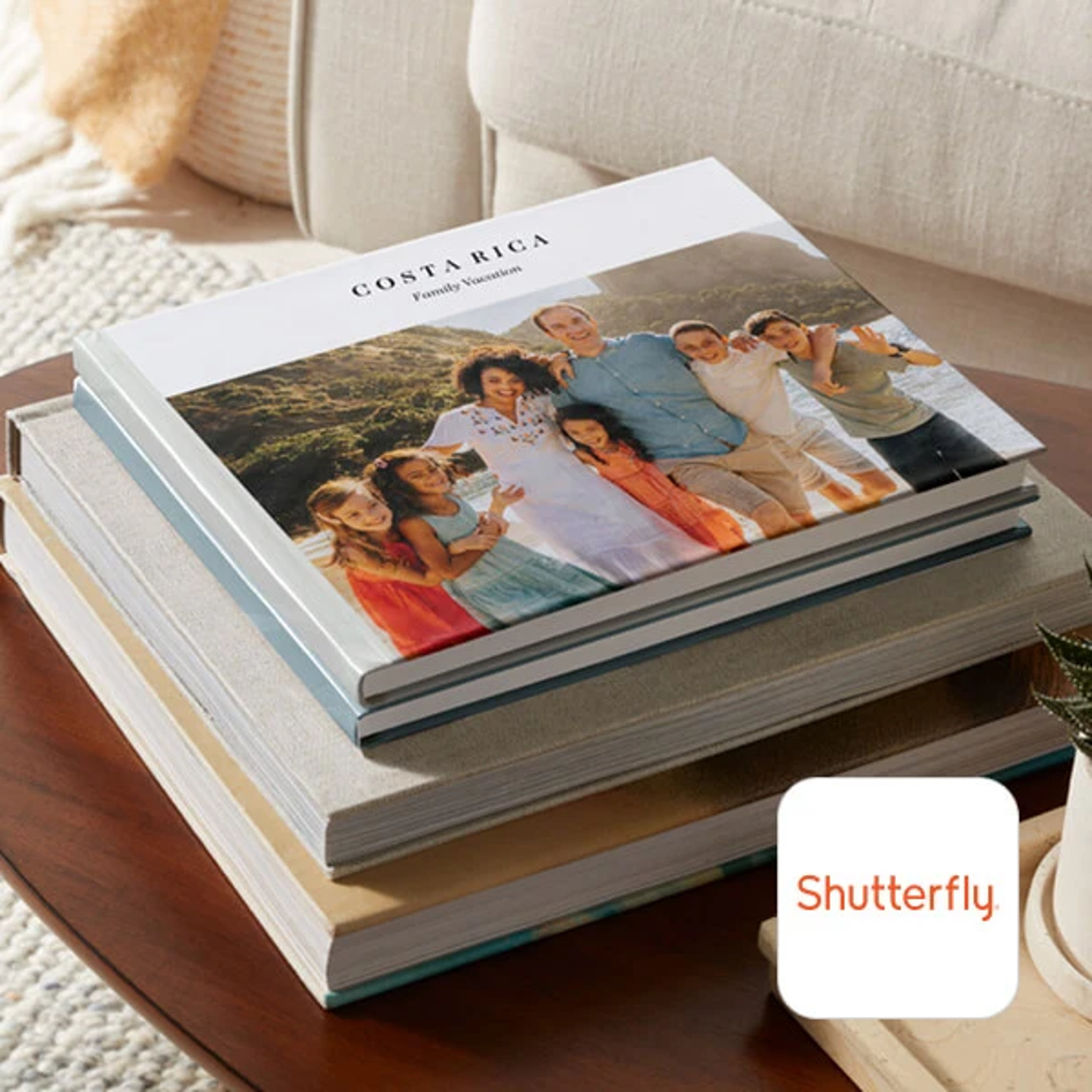 A stack of photo books on a wooden table; the top book displays a cover photo of a smiling family on a beach and the text 'COSTA RICA Family Vacation', with the Shutterfly logo visible in the bottom right corner.