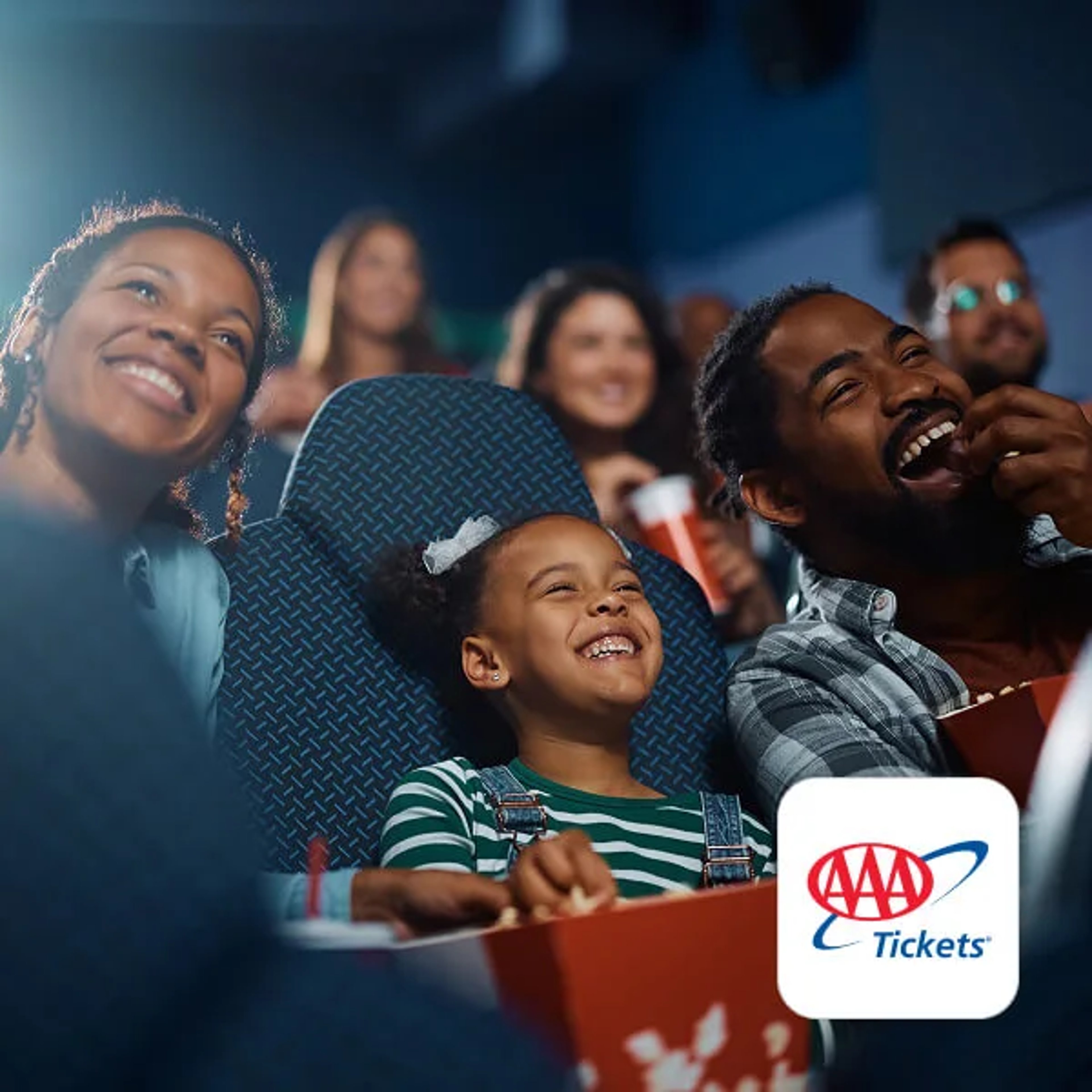 A group of people, including adults and a child, laughing and watching a movie in a theater while eating popcorn, with the AAA Tickets logo in the bottom right corner.