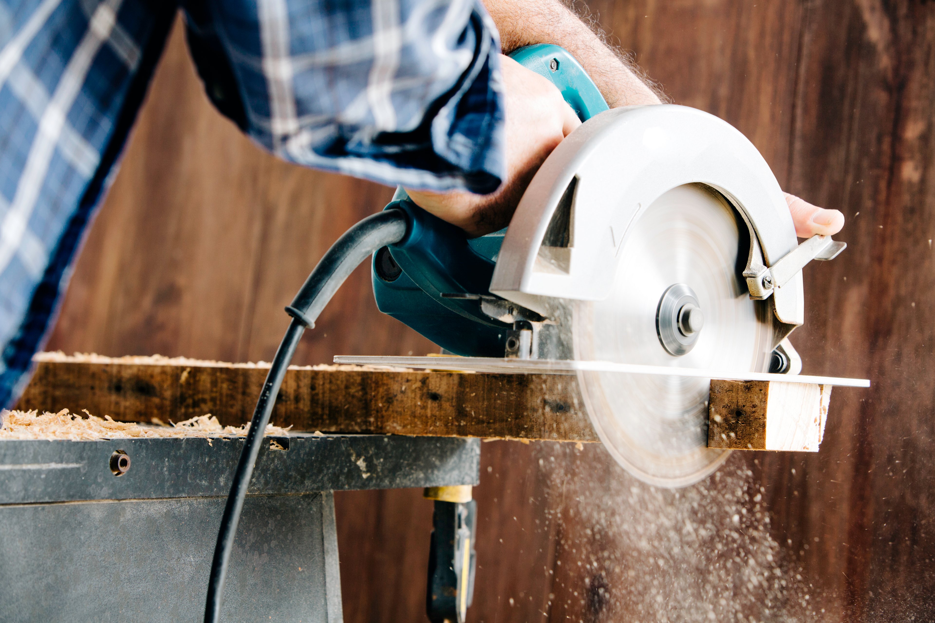 Man in blue plaid shirt finishing a plant of wood on an electric circular saw