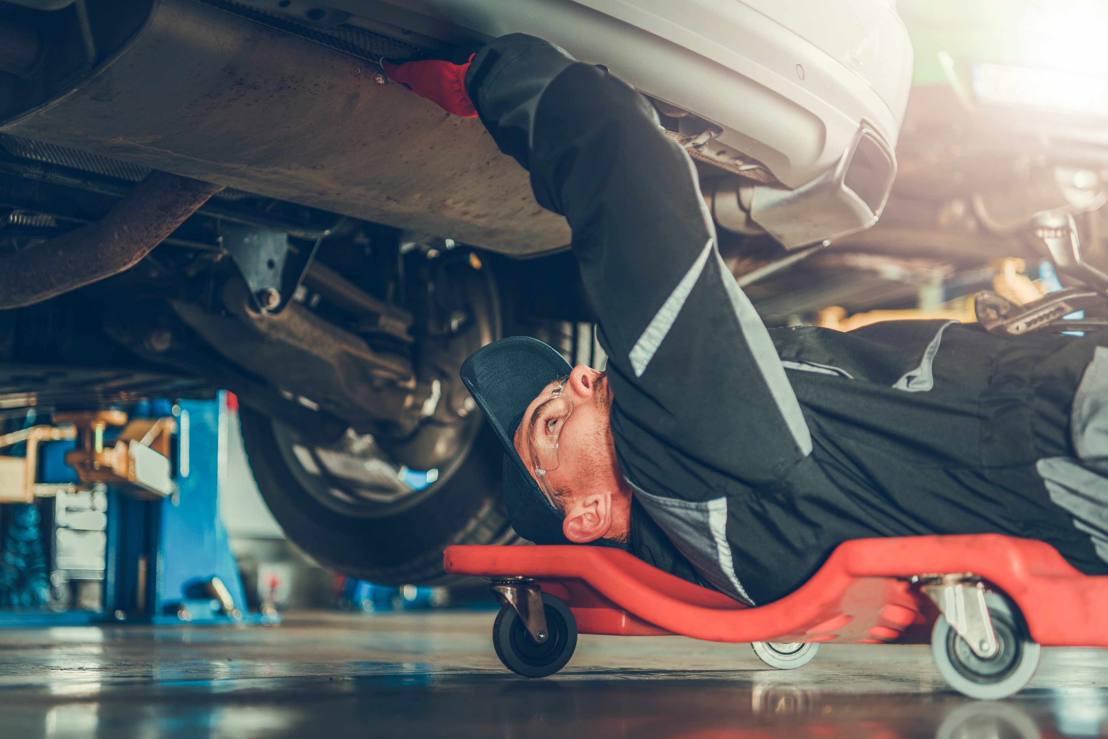 Car mechanic under the car on the mechanics creeper fixing modern vehicle exhaust system
