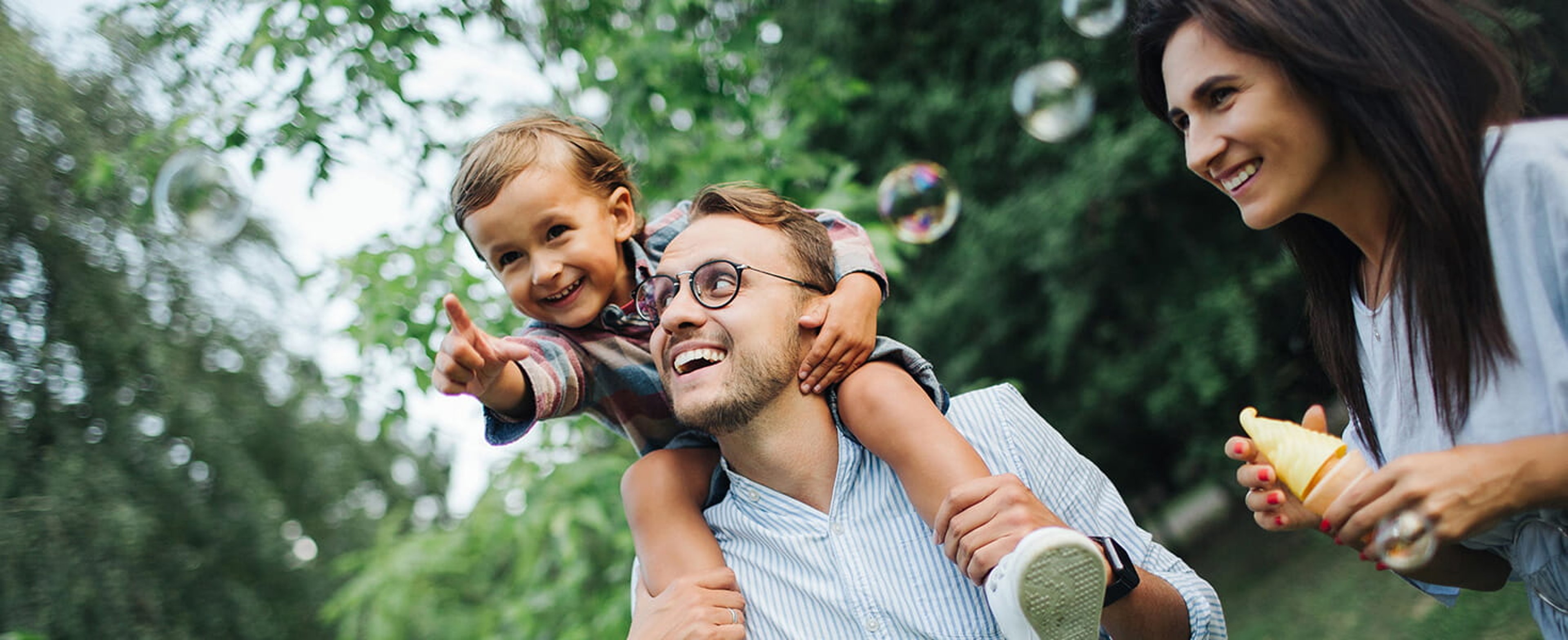 Father carrying happy child on his shoulders while smiling mother watches
