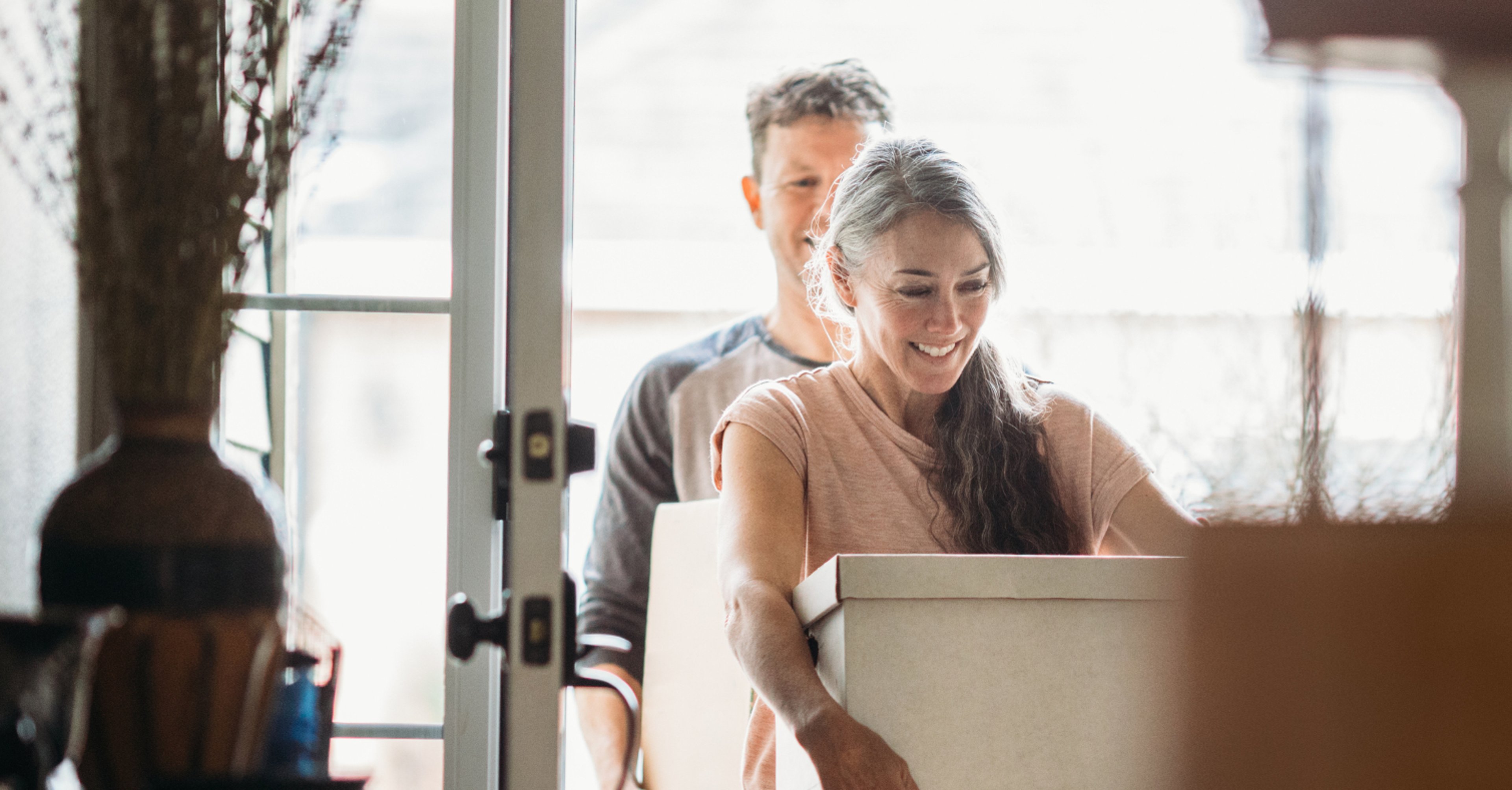 Smiling couple carrying moving boxes through the front door of their newly purchased home