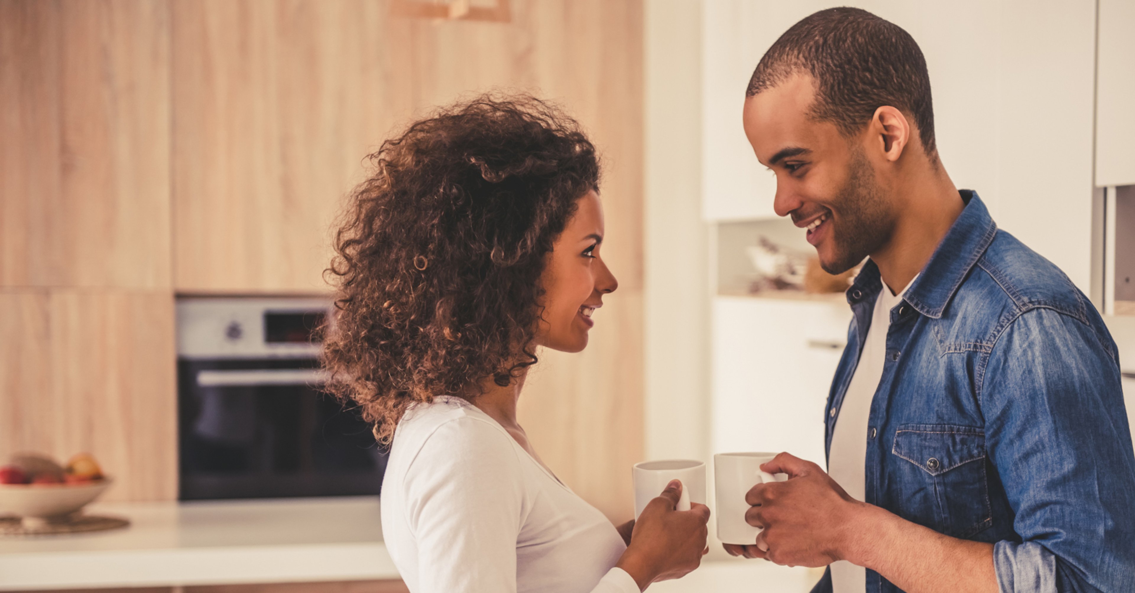 Newlywed couple looking at each other and smiling while drinking coffee in their kitchen