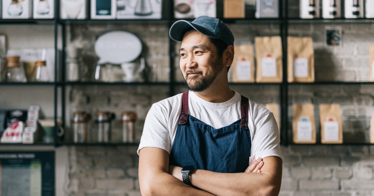 Smiling man and shop owner with apron standing in front of stocked shelves