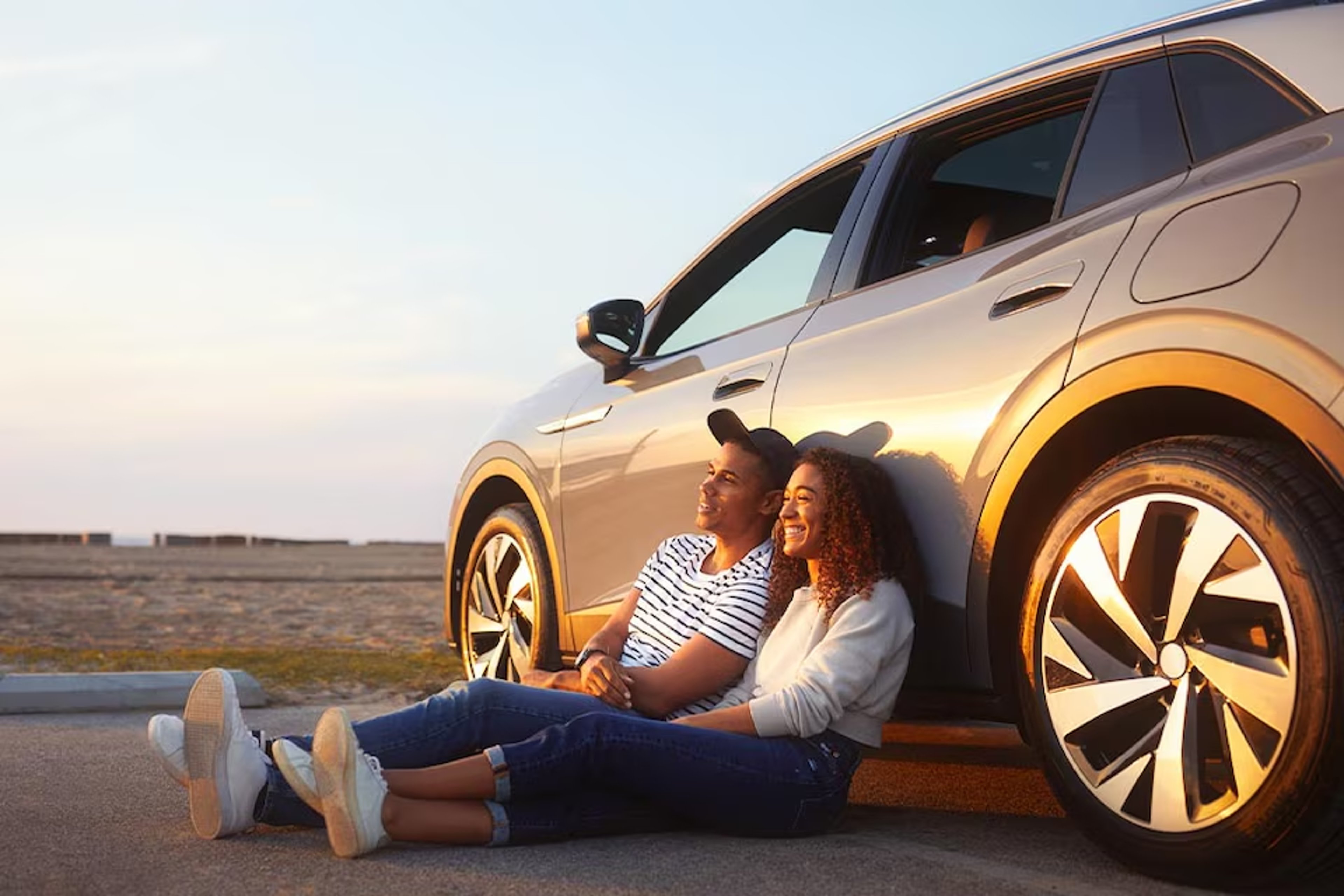 Couple seated on ground, against their car, watching a sunset at the beach