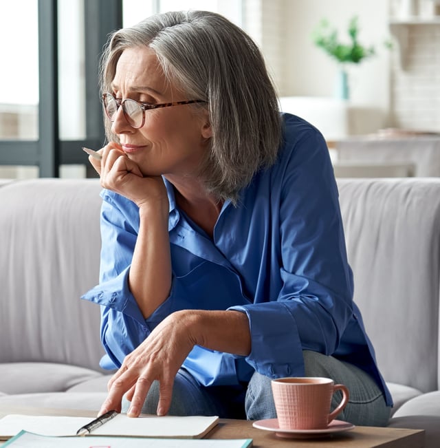 Mature woman with silver hair working at desk with cup of tea