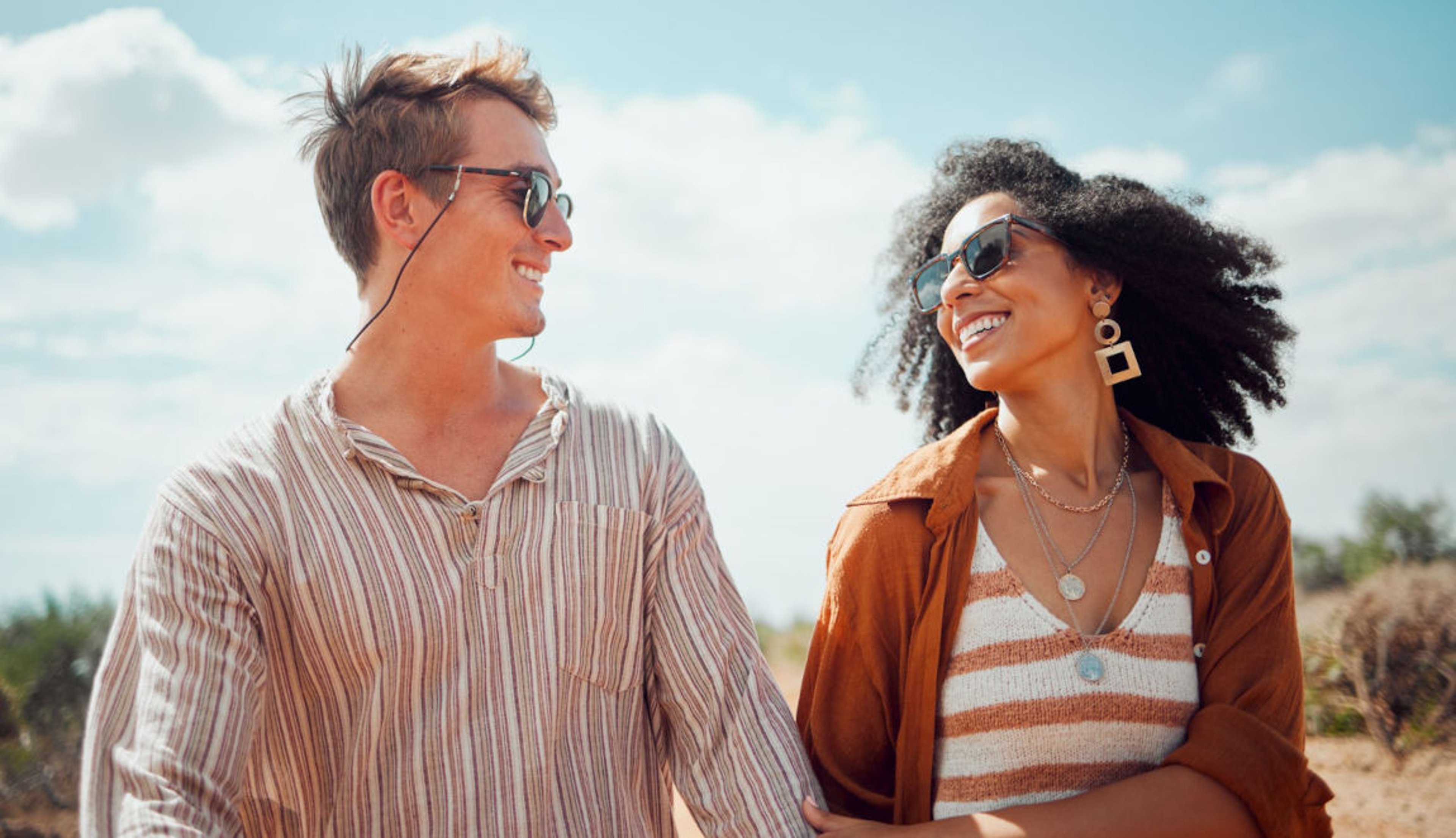 Man and woman couple with sunglasses smiling at each other on a sunny beach