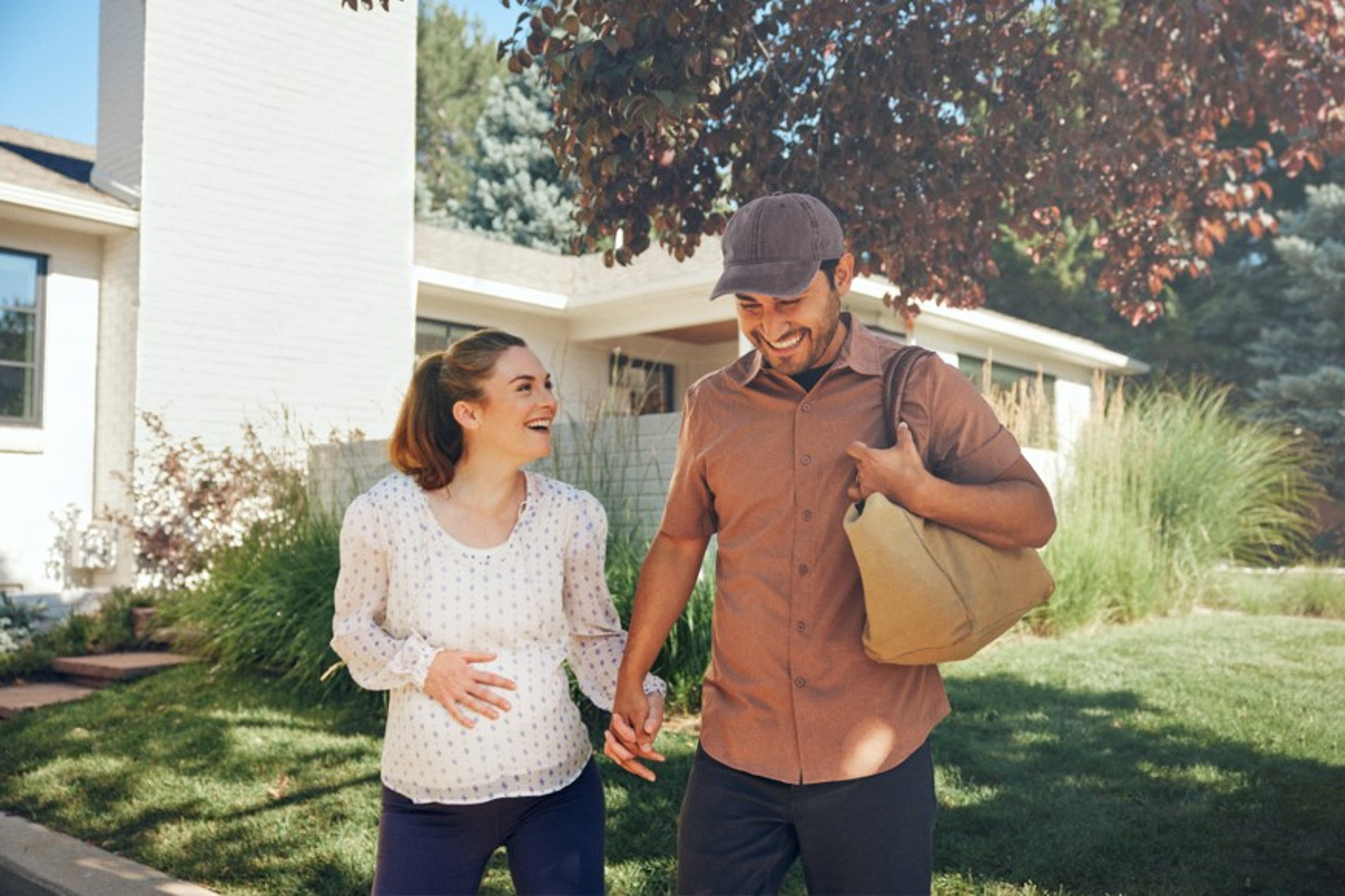 Expecting couple smiling in front yard of home