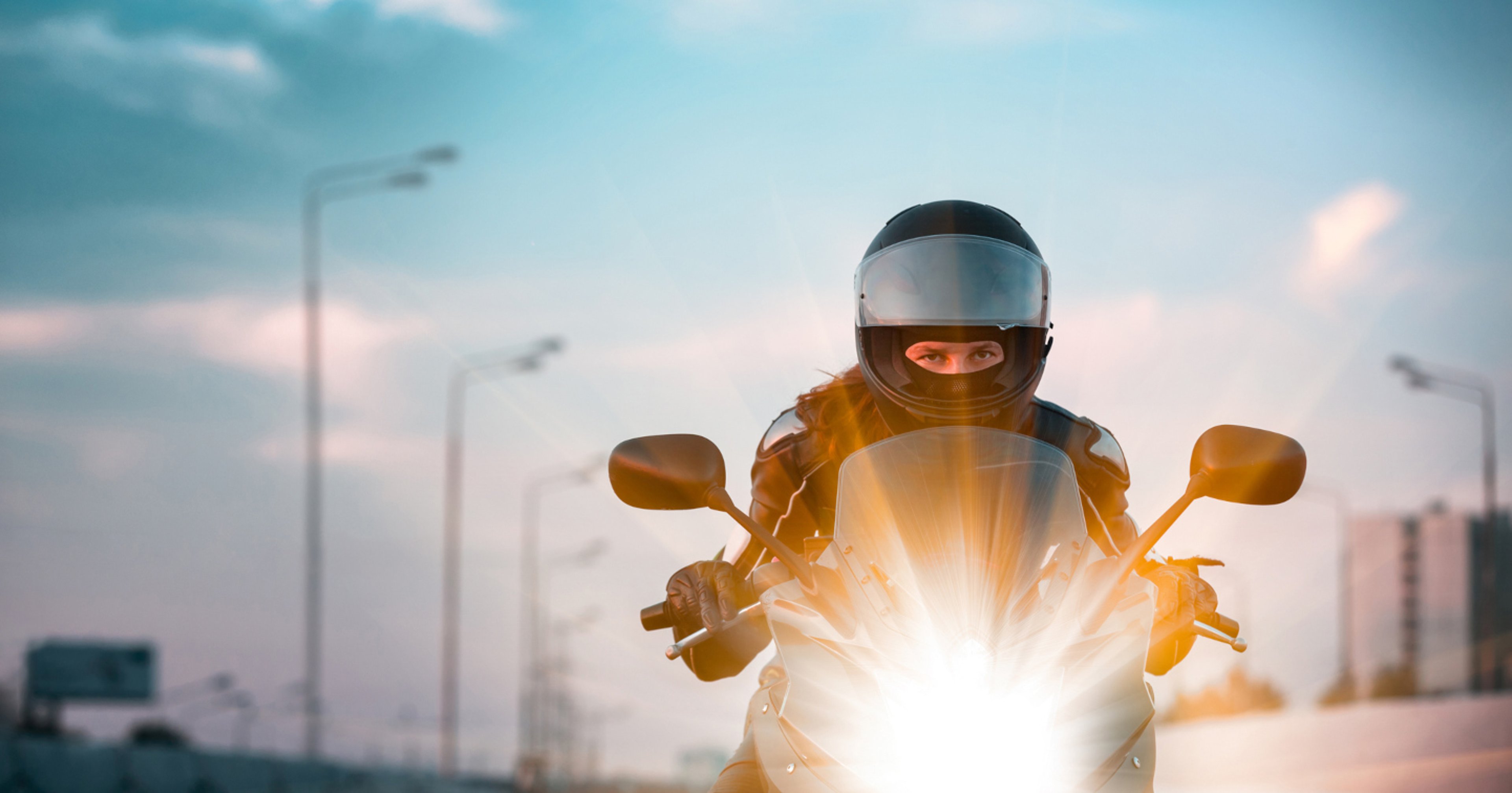 AAA Specialty Lines Motorcycle Insurance Woman riding motorcycle with bright headlights on busy highway at sunrise
