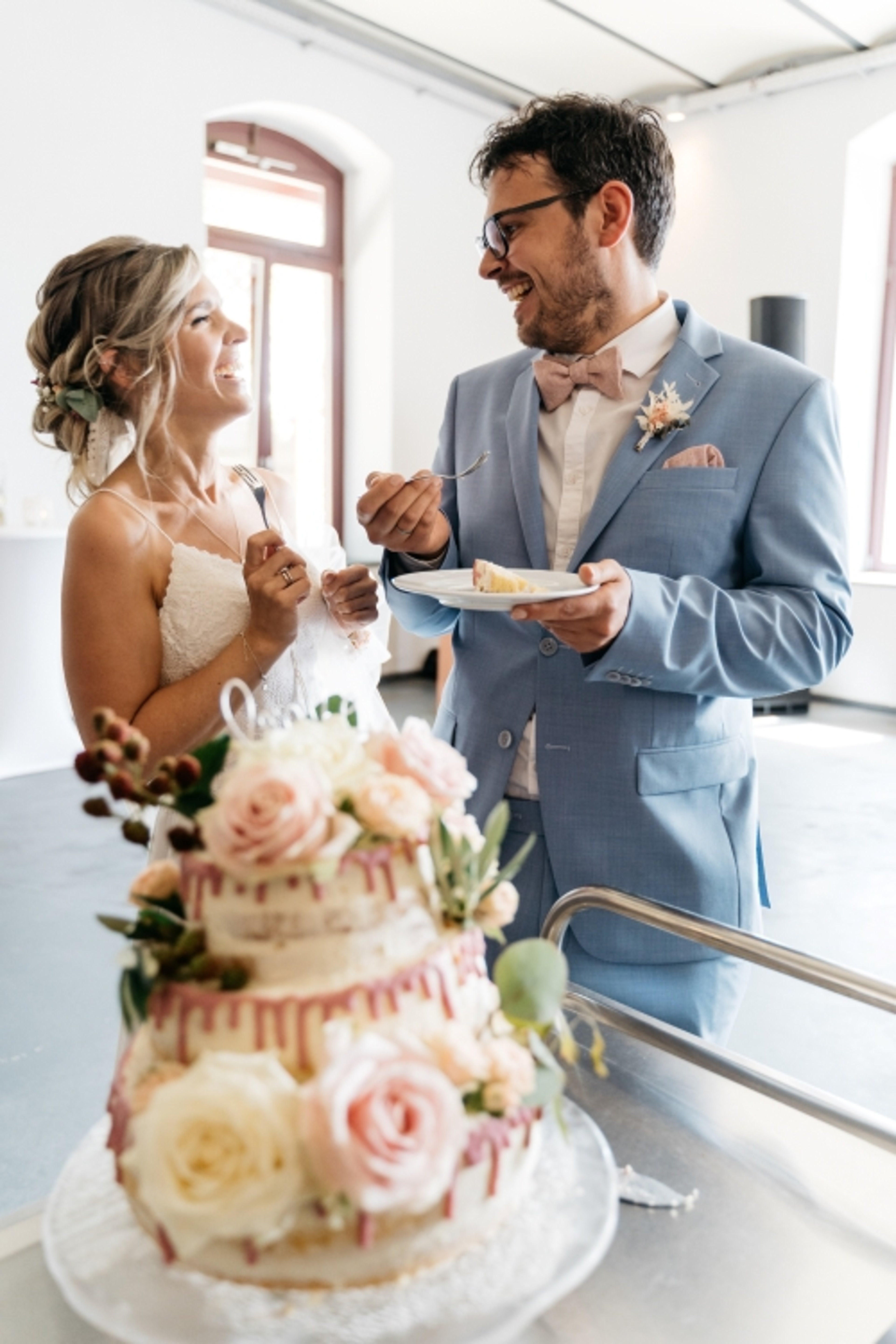 Bride and groom looking at each other in front of wedding cake with flowers