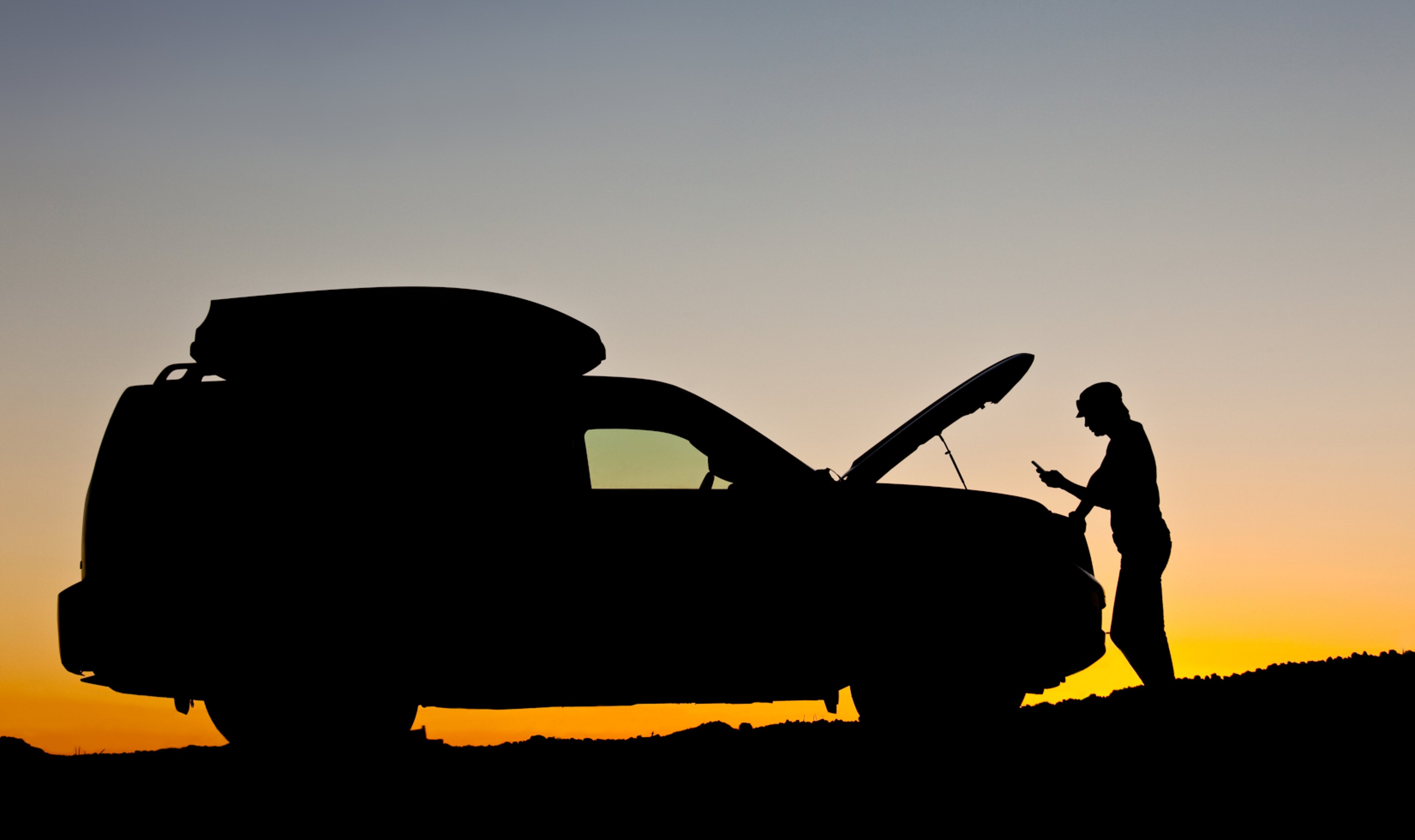 Silhouette of a woman looking at her phone leaned against a disabled vehicle