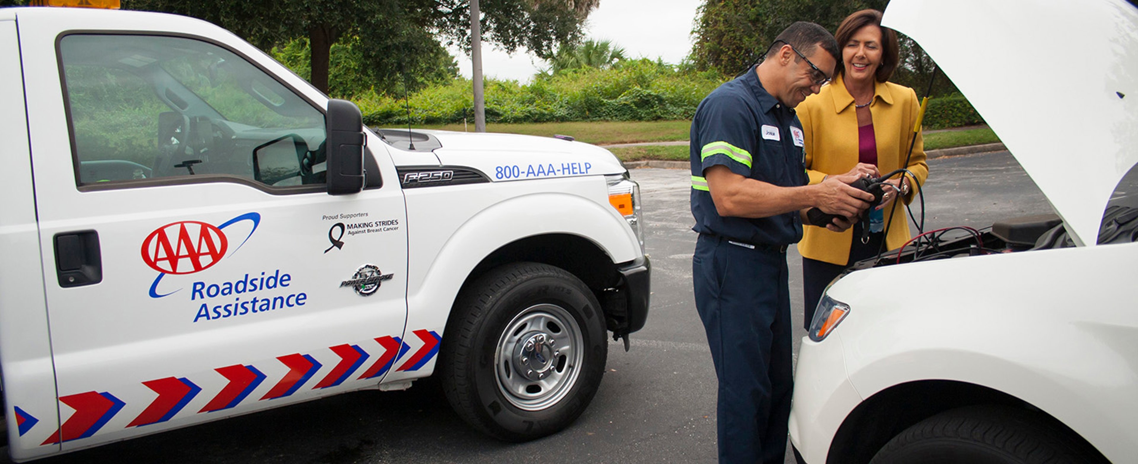 AAA Roadside Assistance truck parked infront of service man and woman testing battery in white car with hood up