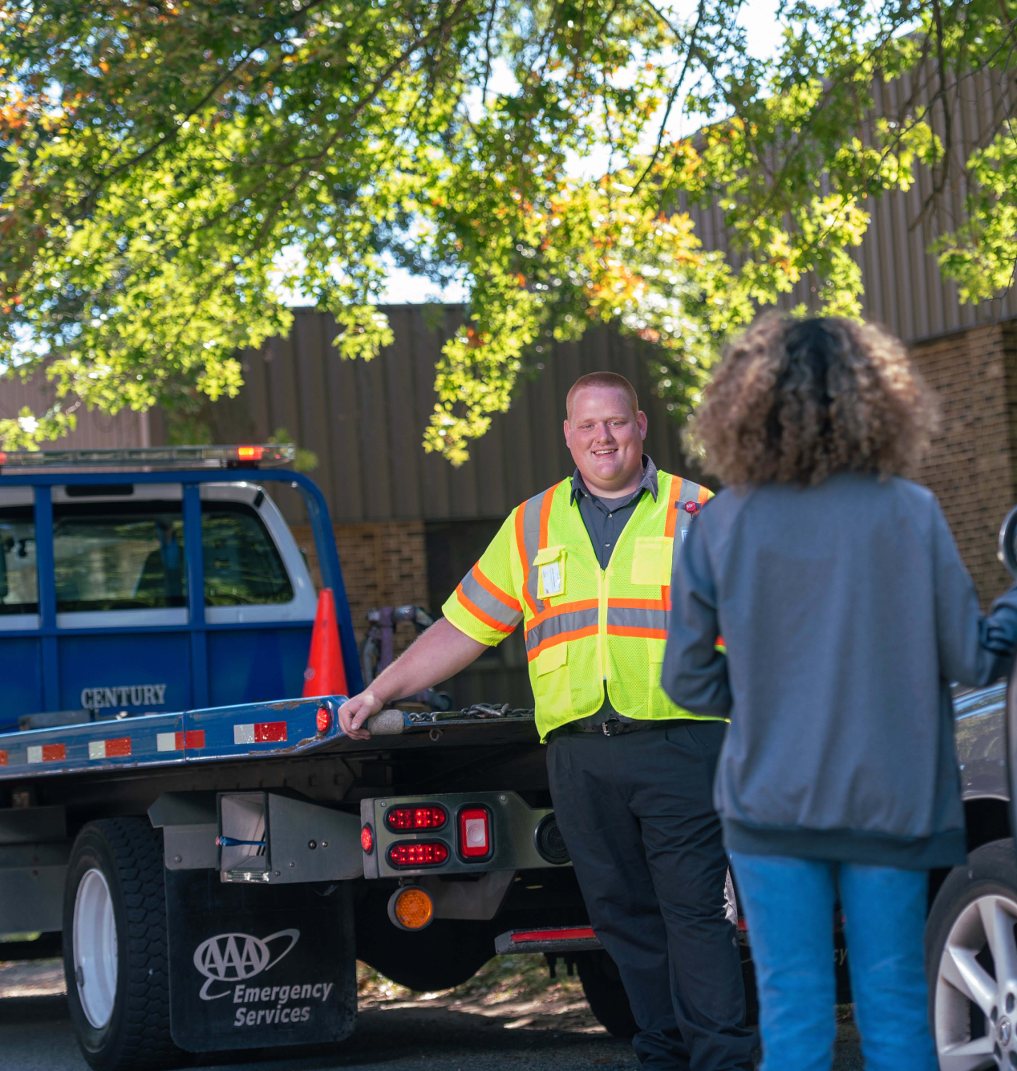 AAA technician with flatbed truck providing roadside assistance towing to woman on the side of the road