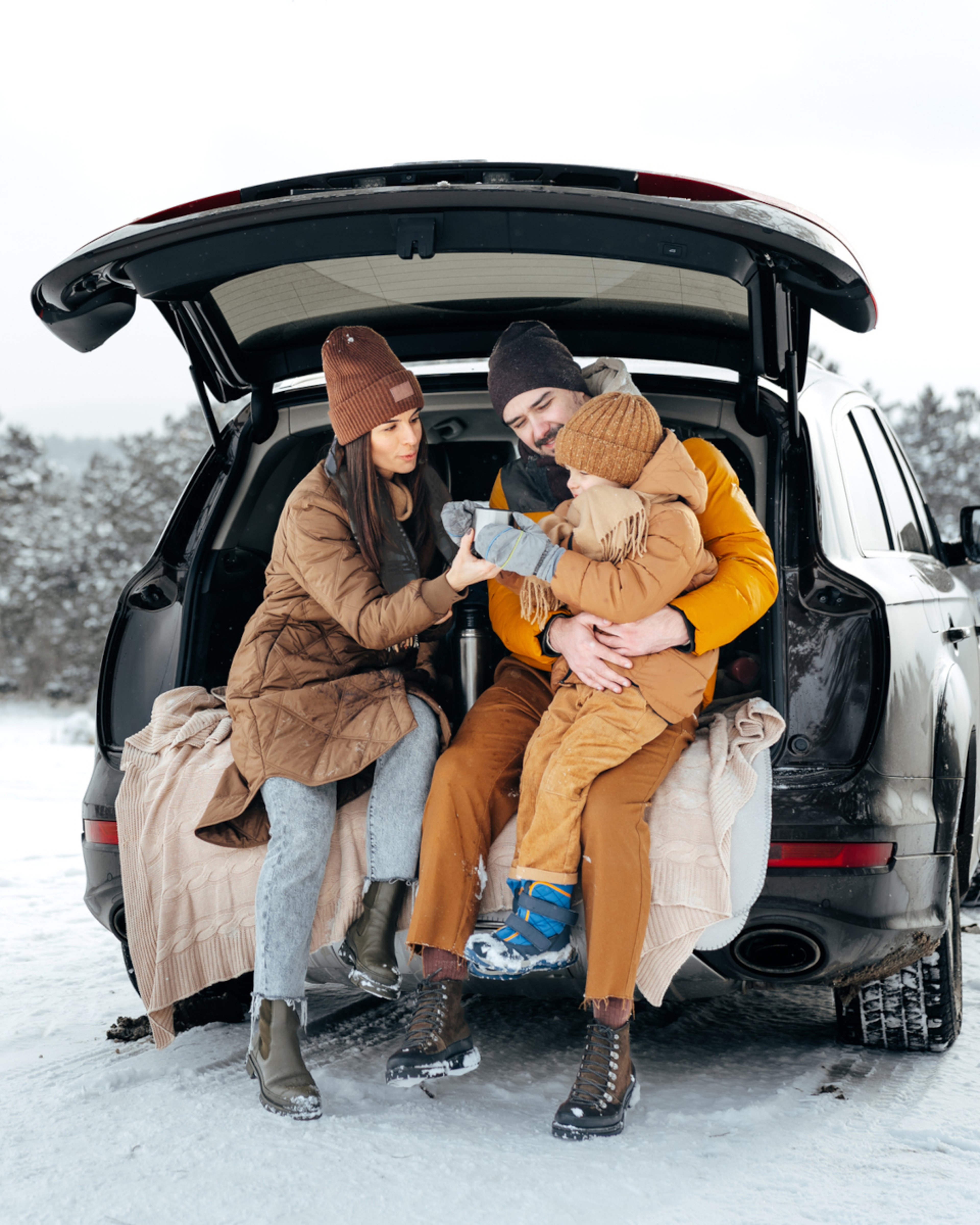 Family of three sitting in trunk of car on a snowy day