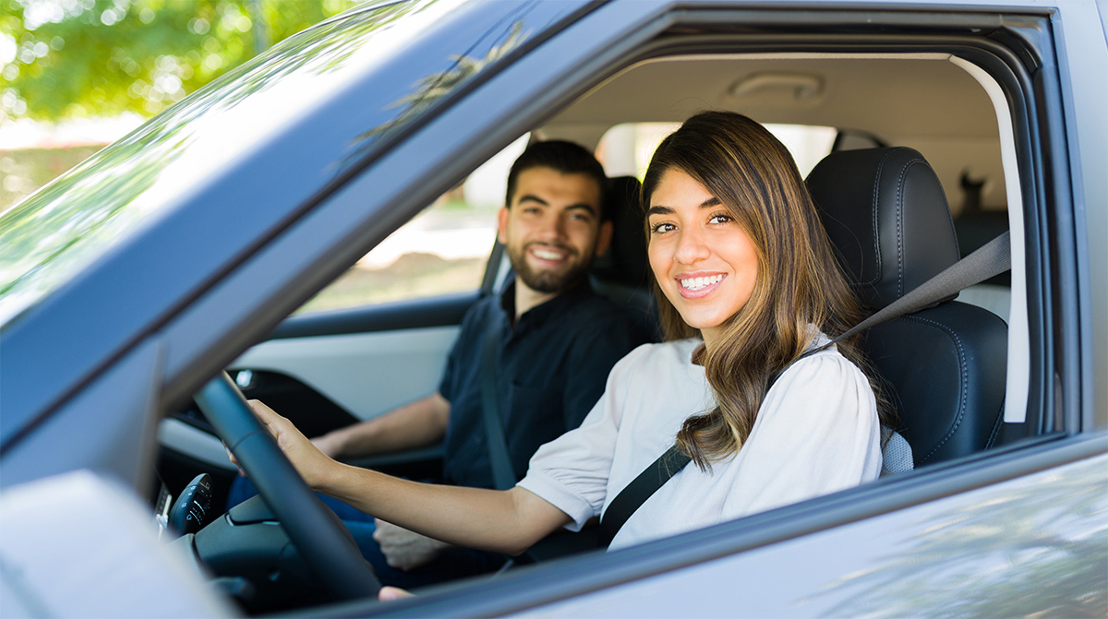 Happy woman in driver seat of car while her male passenger smiles in the background