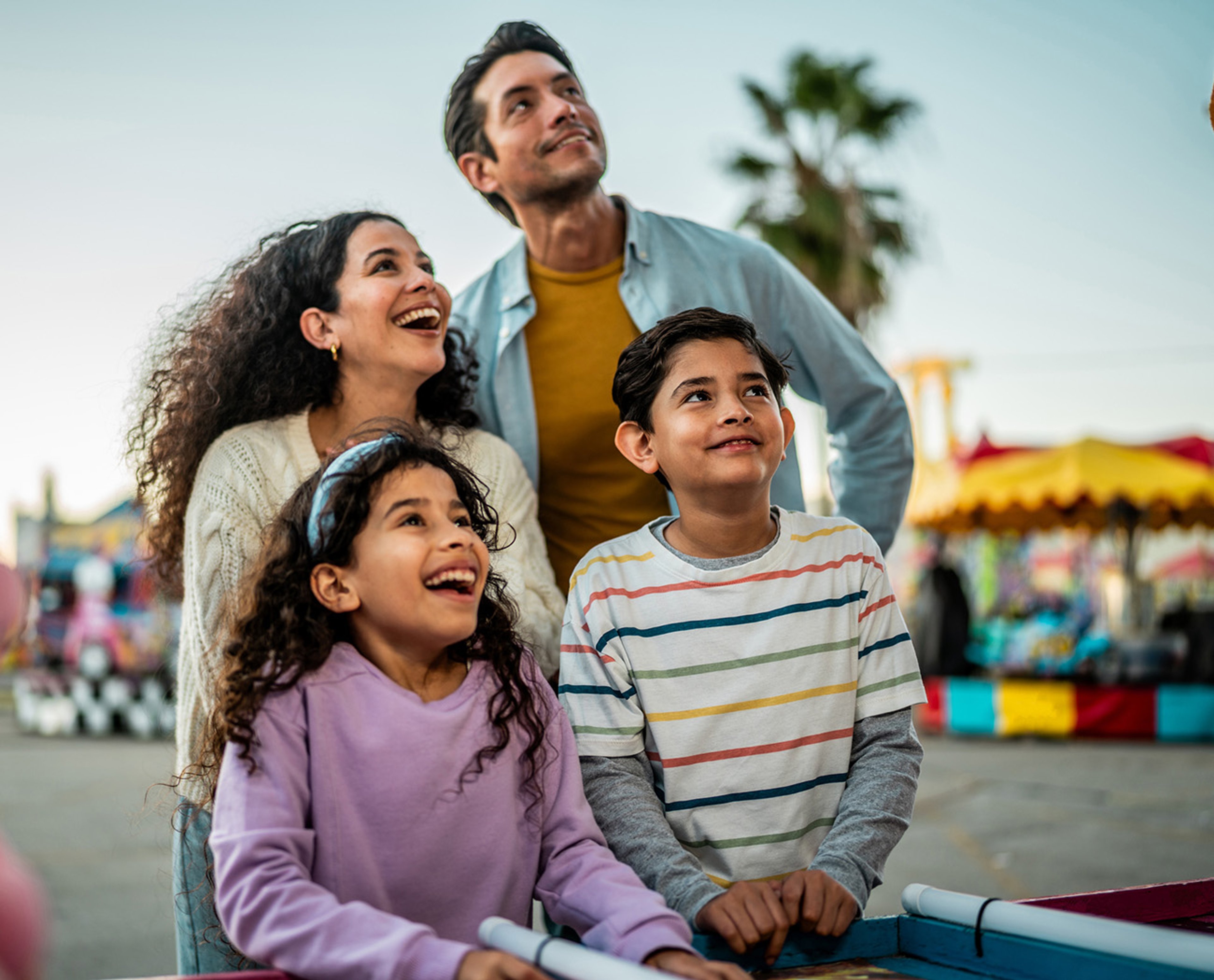 Smiling family of four looking up at ride at amusement park