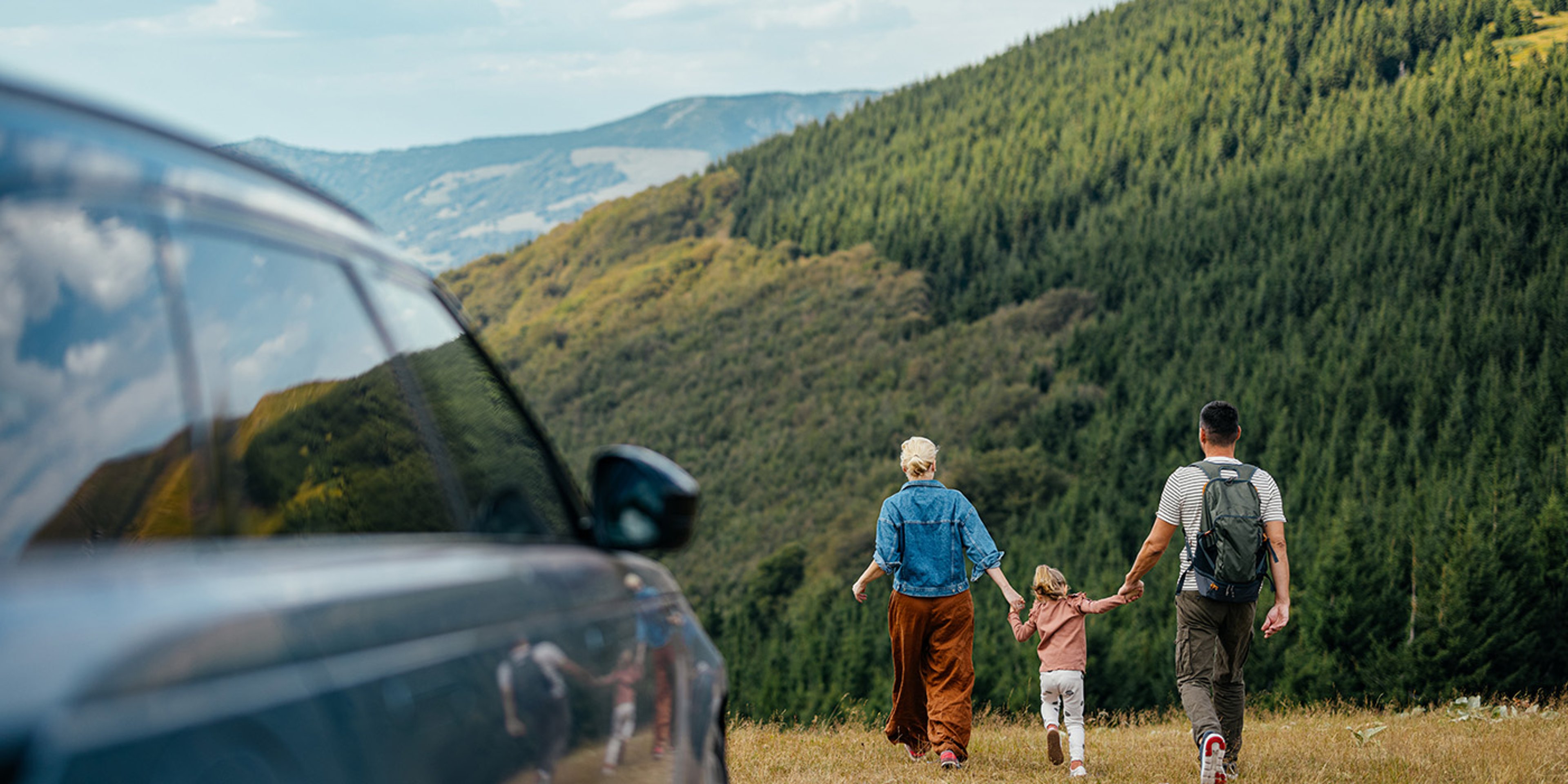 Family of three walking on mountain hike with their utility vehicle in the foreground