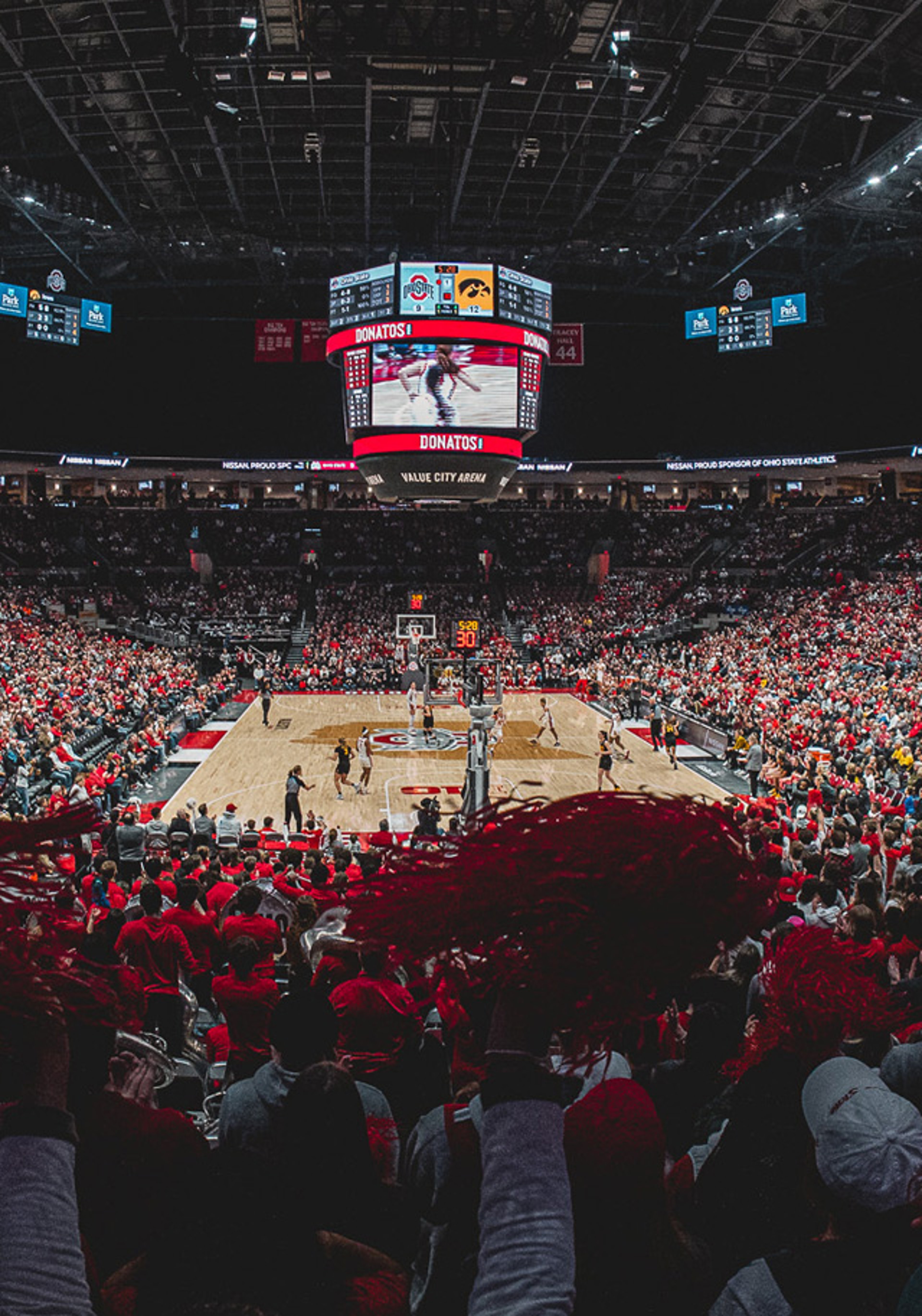 A packed arena during a college basketball game with fans in red shirts.