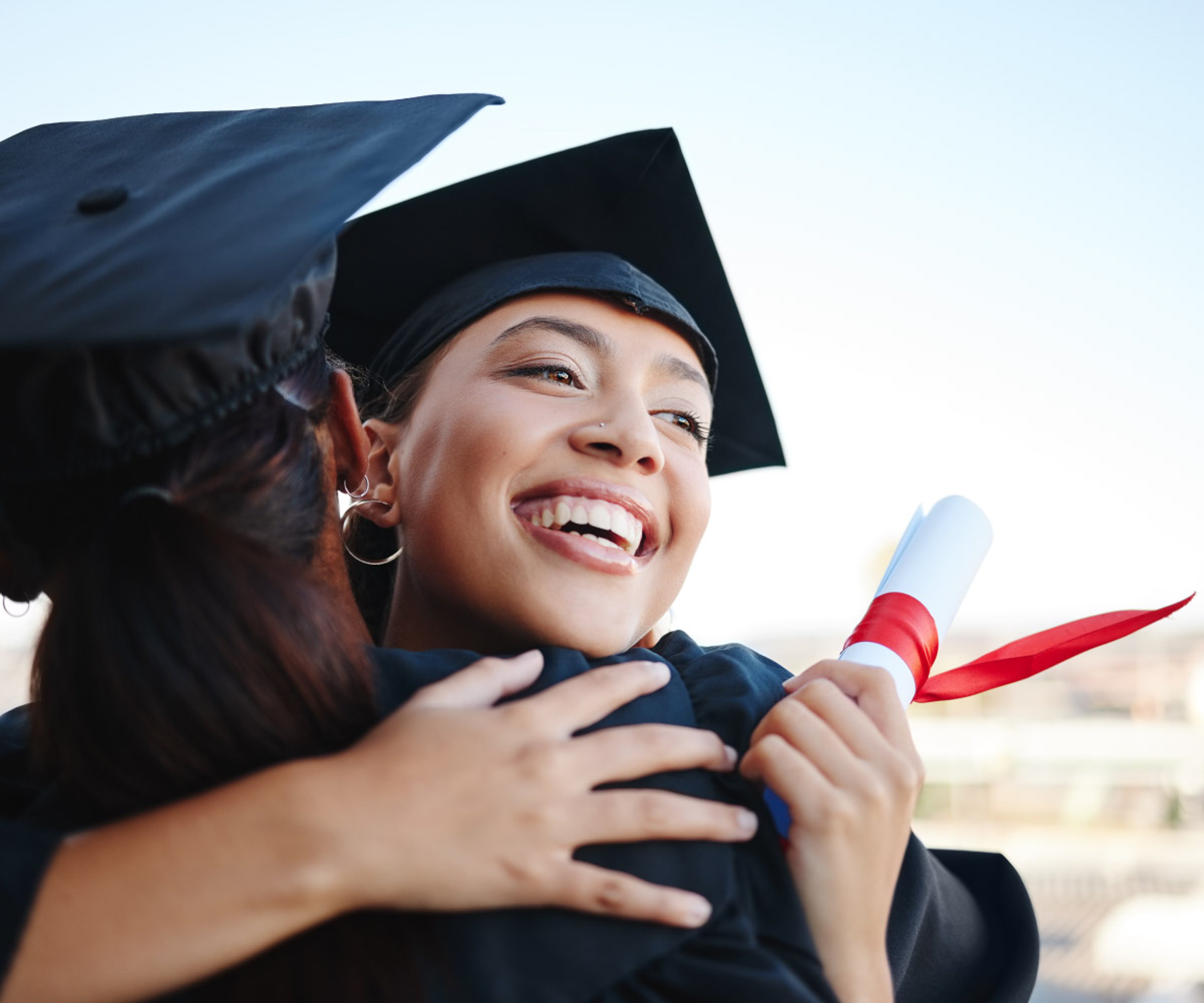 A recently graduated student hugging their friend and smiling with their paper degree