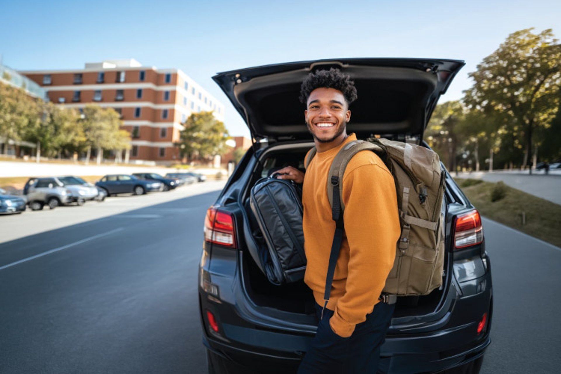 A grad student posing outside of their car trunk with luggage 