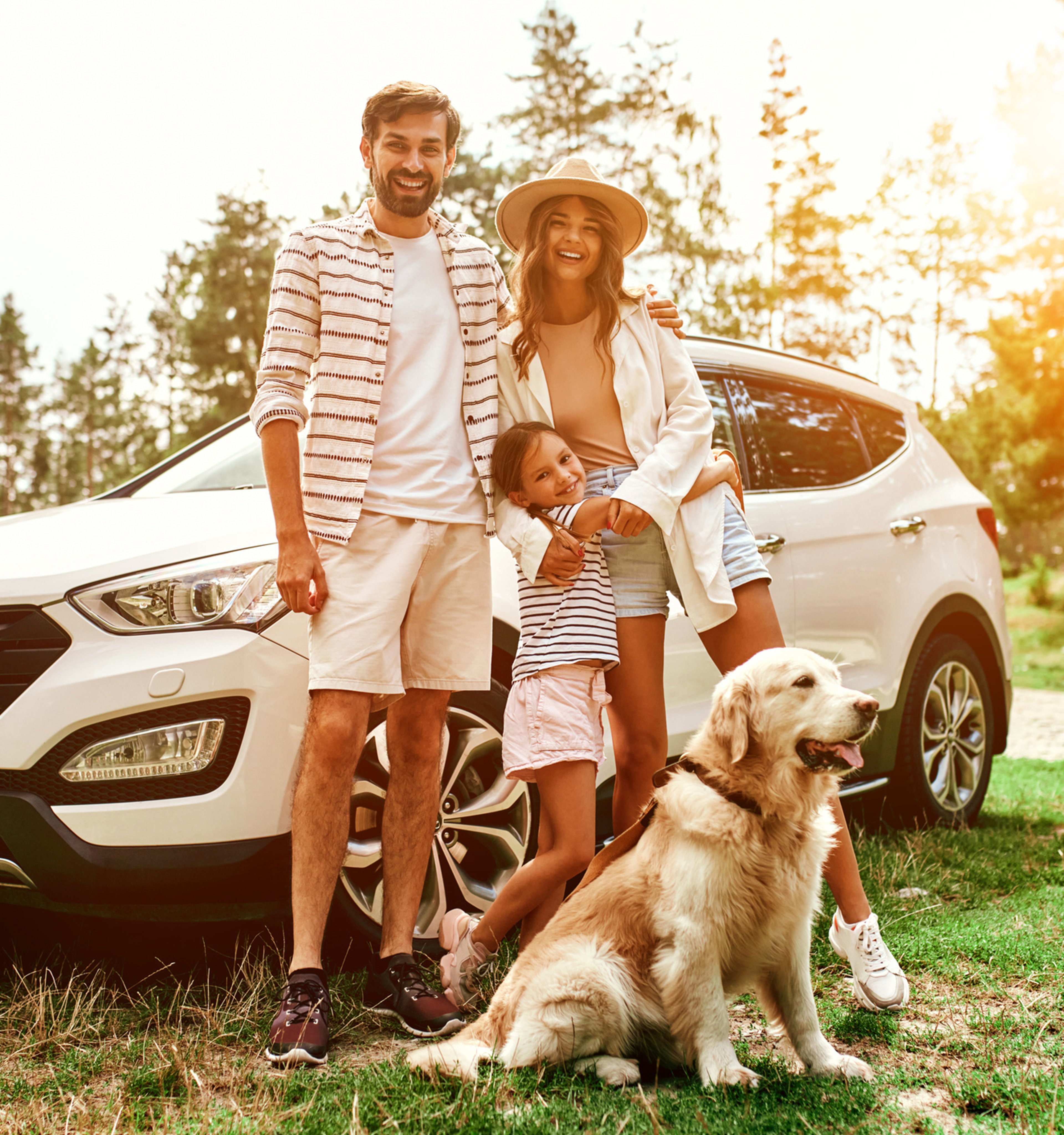 Father, mother, daughter and family dog standing outside in front of car