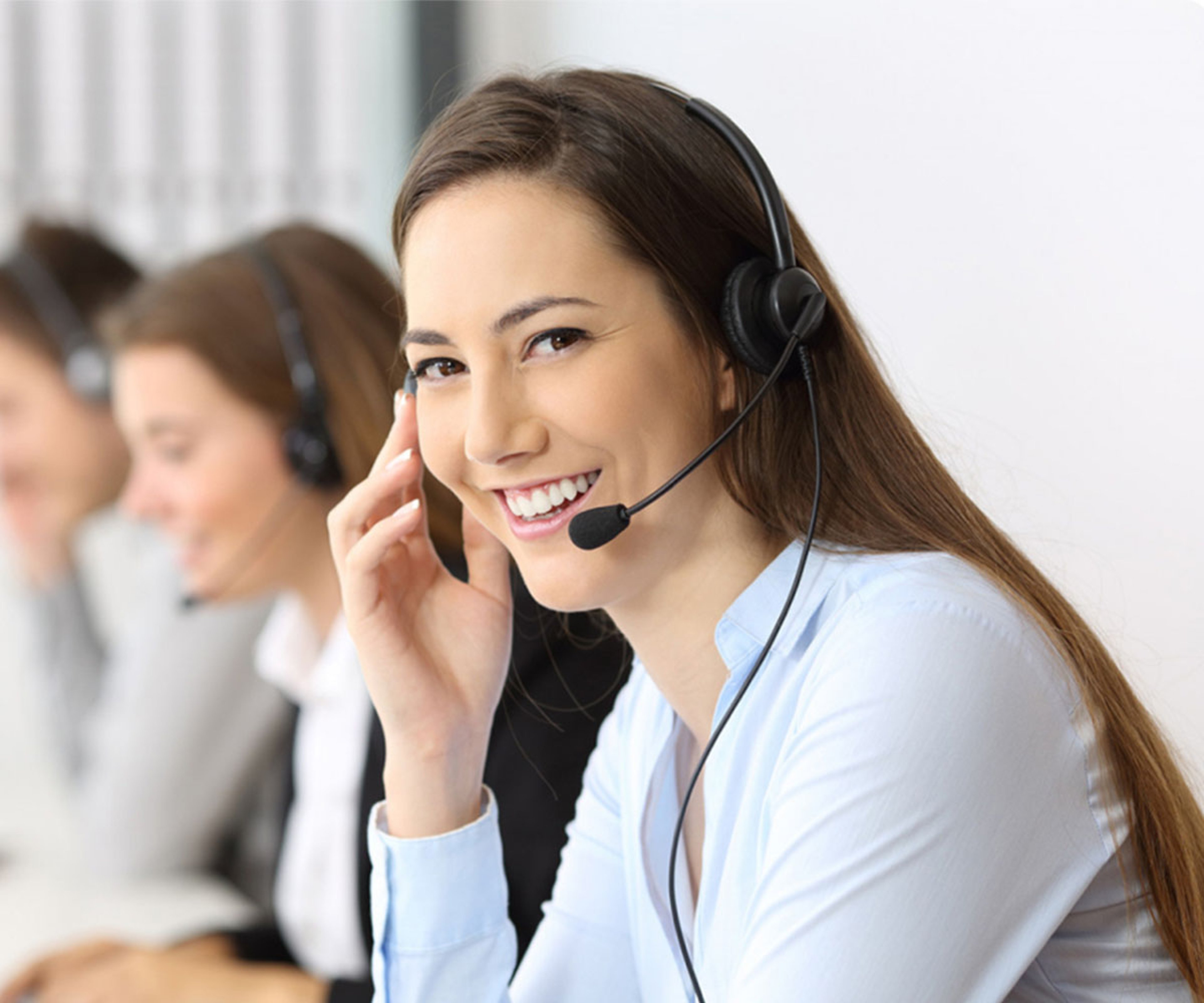Smiling woman with a headset at a call center, with two people working in the background