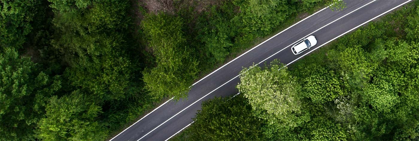 Aerial view of a winding road through a dense green forest with a white car driving on it