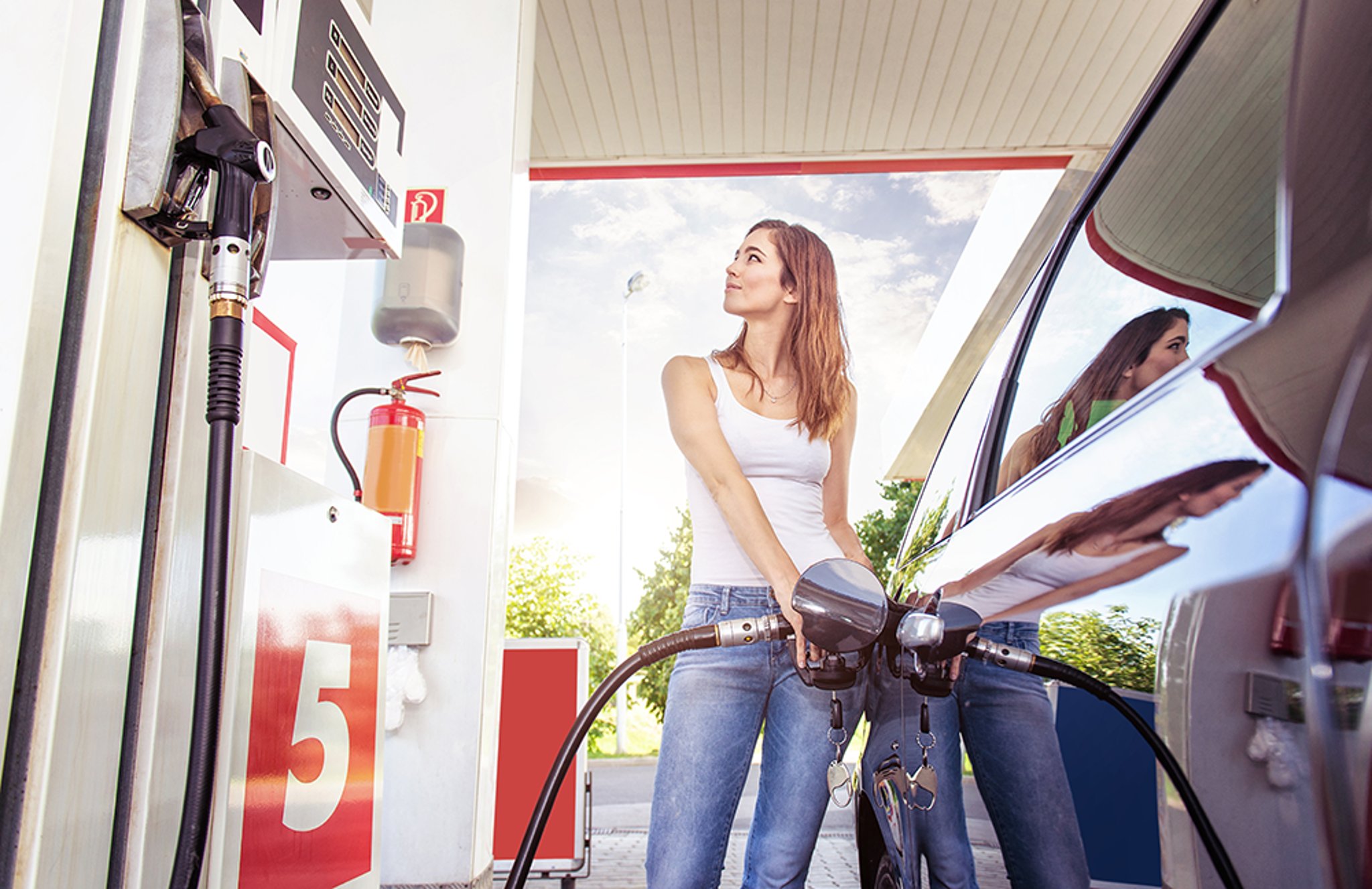 A woman refueling her car at a gas station pump marked with 5.