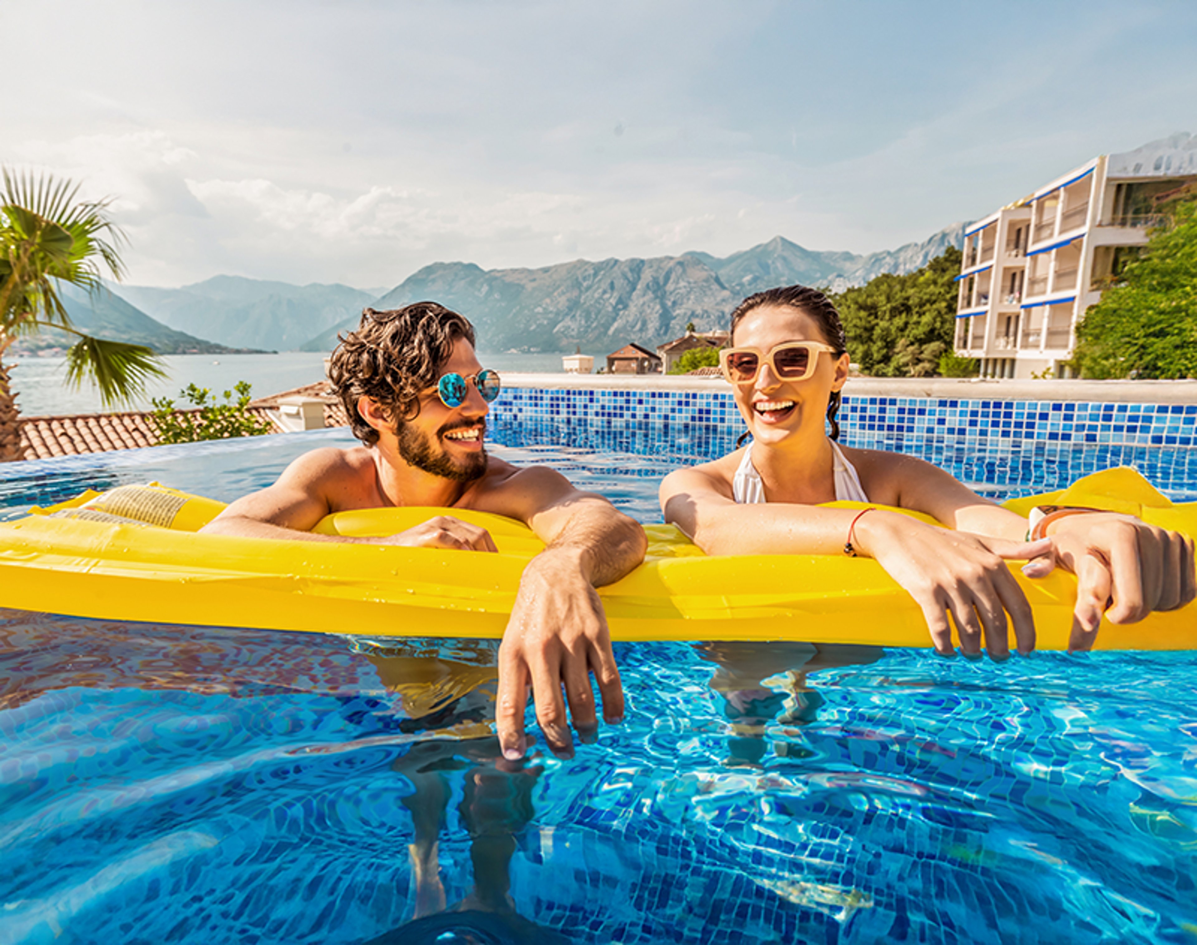 Couple smiling while resting atop pool float in hotel pool
