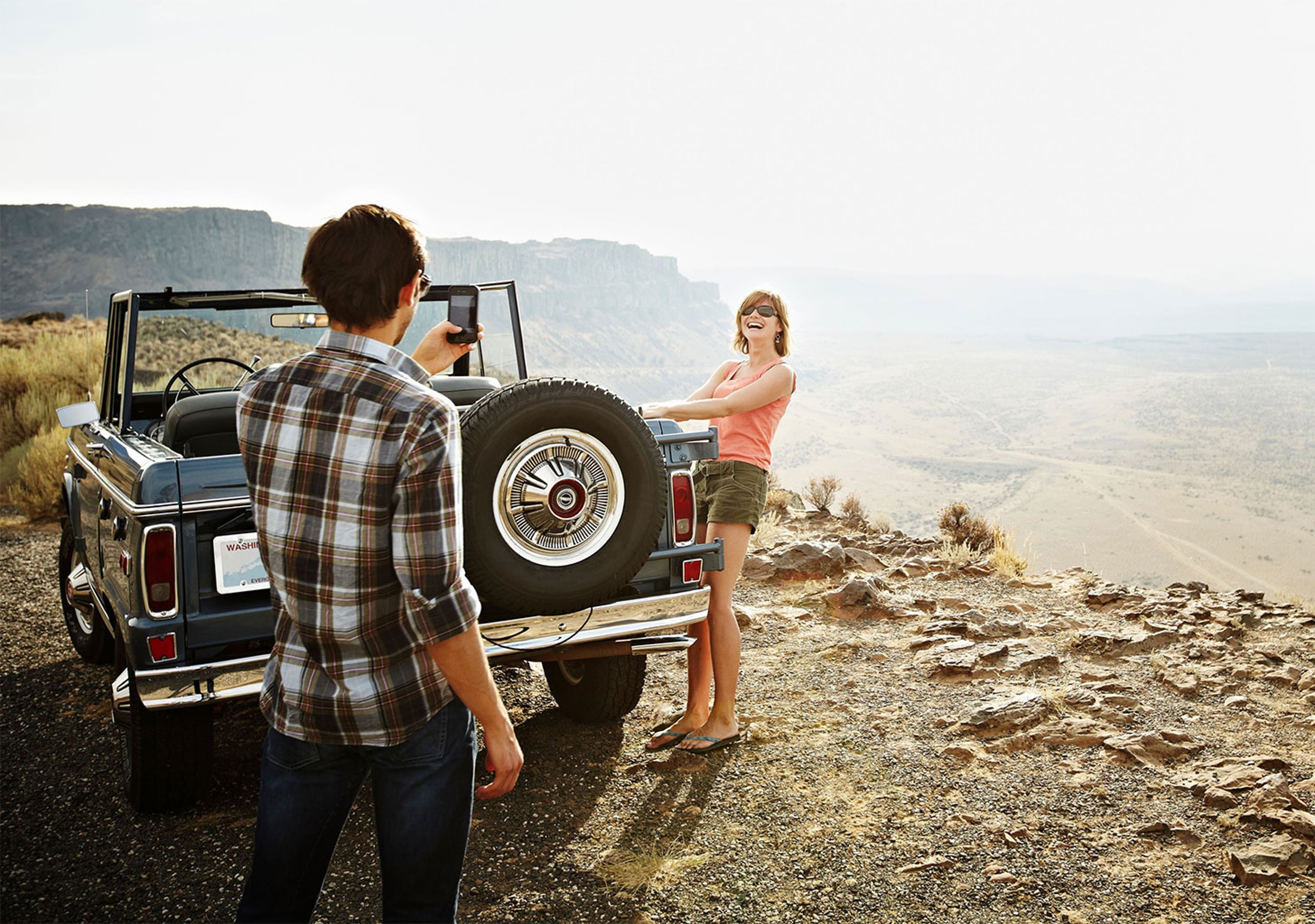 Young couple taking photos over a picturesque canyon outside of their antique Jeep