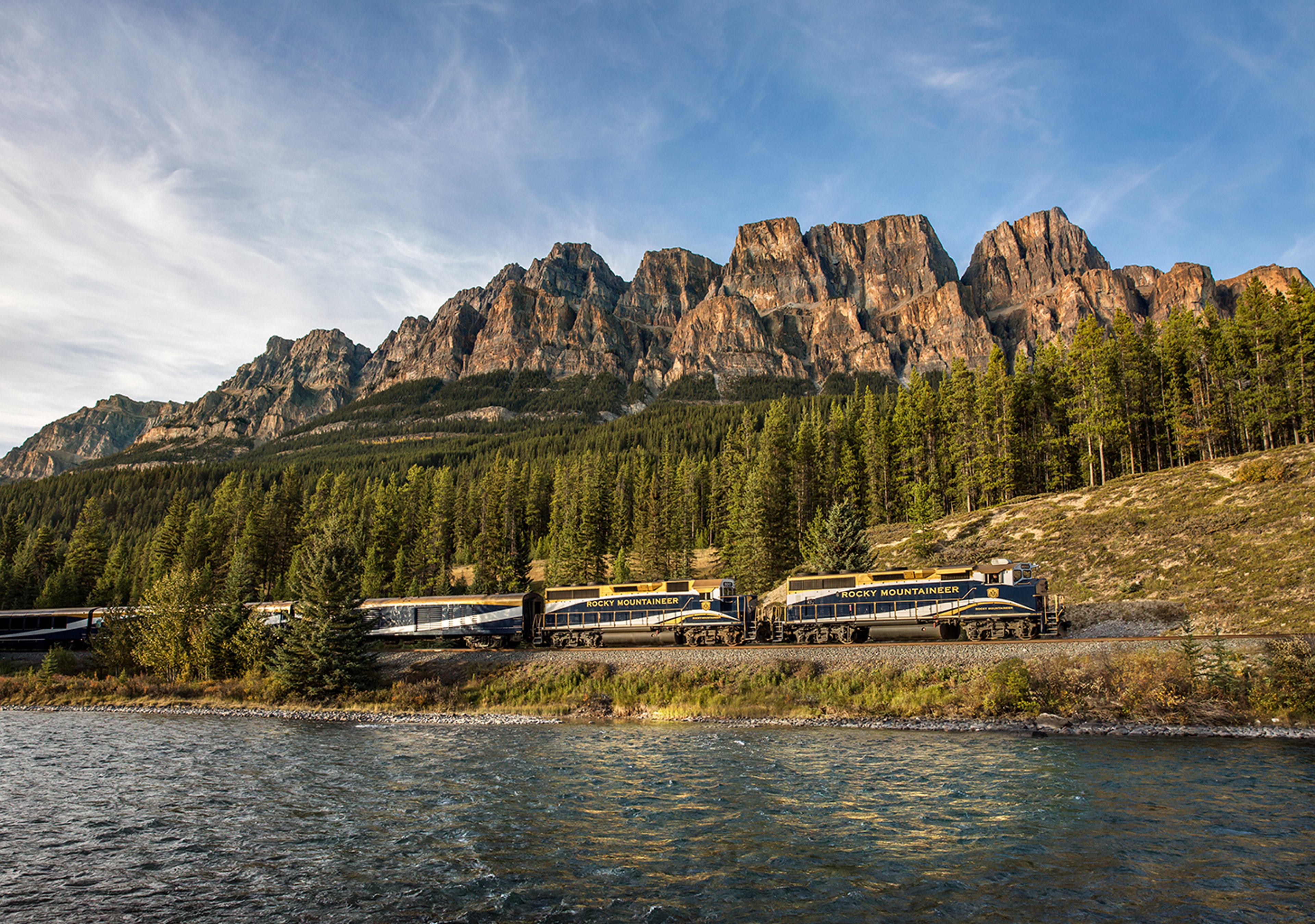 Rocky Mountaineer train traveling with a body of water in the foreground and a mountain range in the background