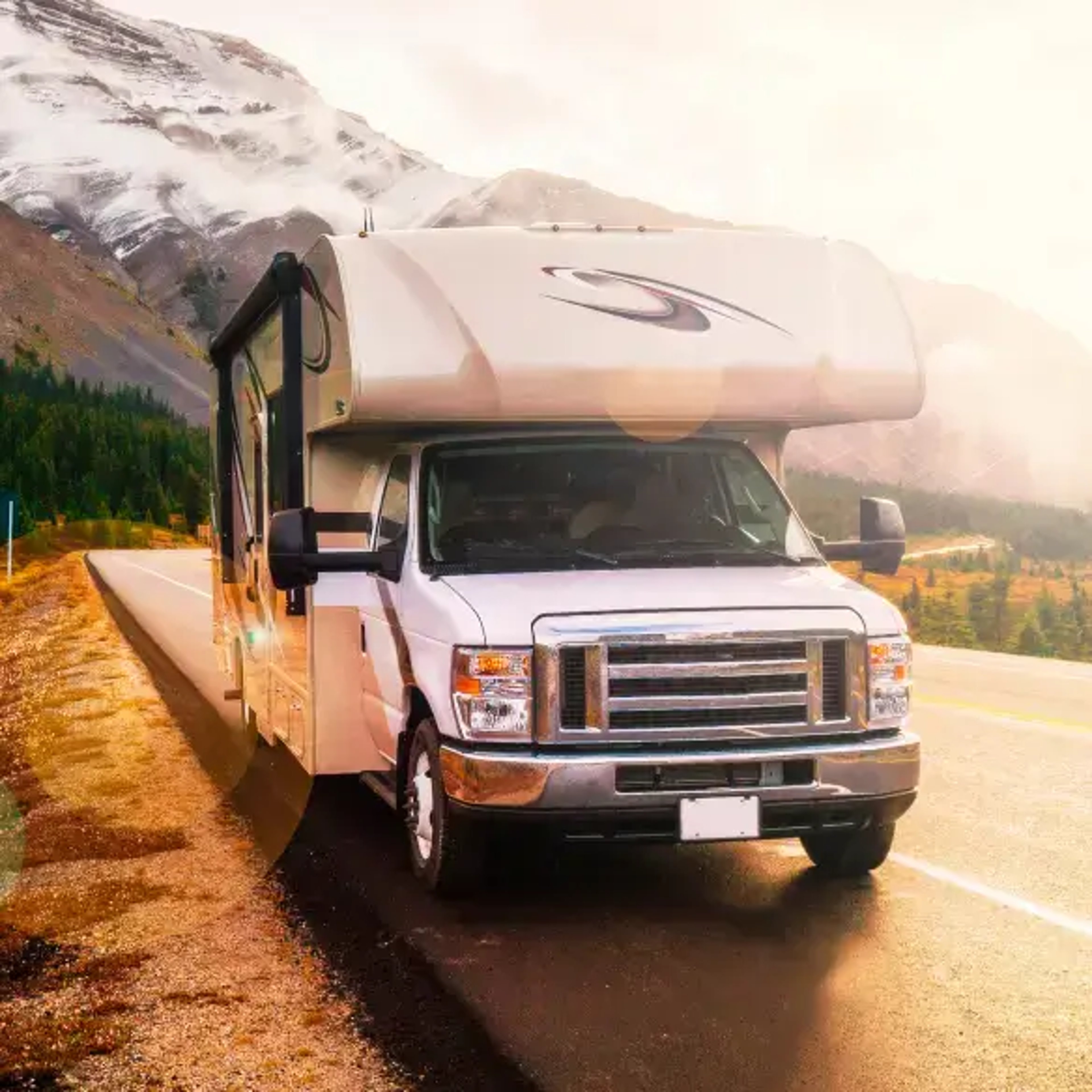 A recreational vehicle (RV) parked on a scenic road surrounded by mountains and trees, with sunlight casting a warm glow over the landscape