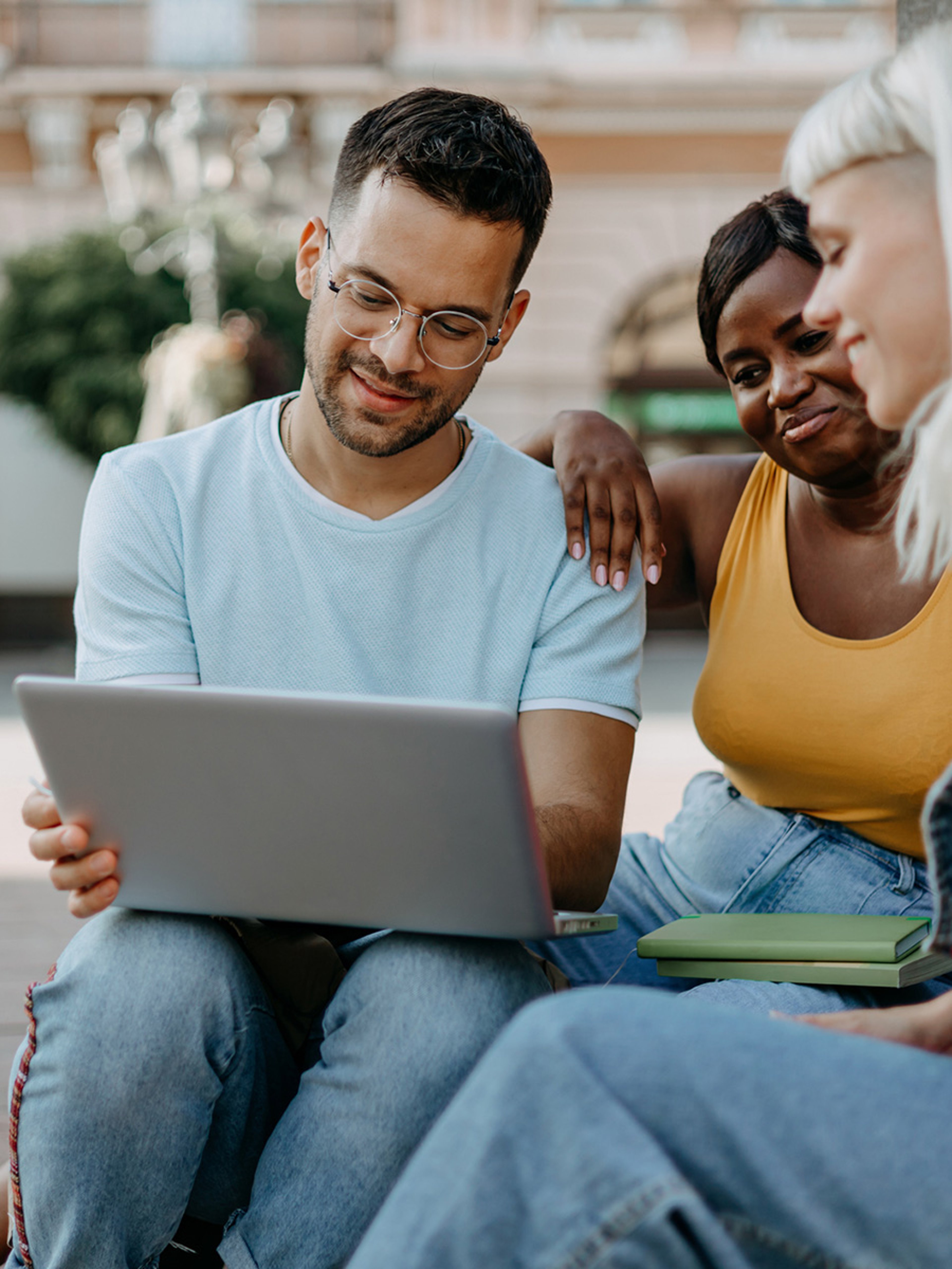 College students sitting in a group on campus smiling and looking at laptop
