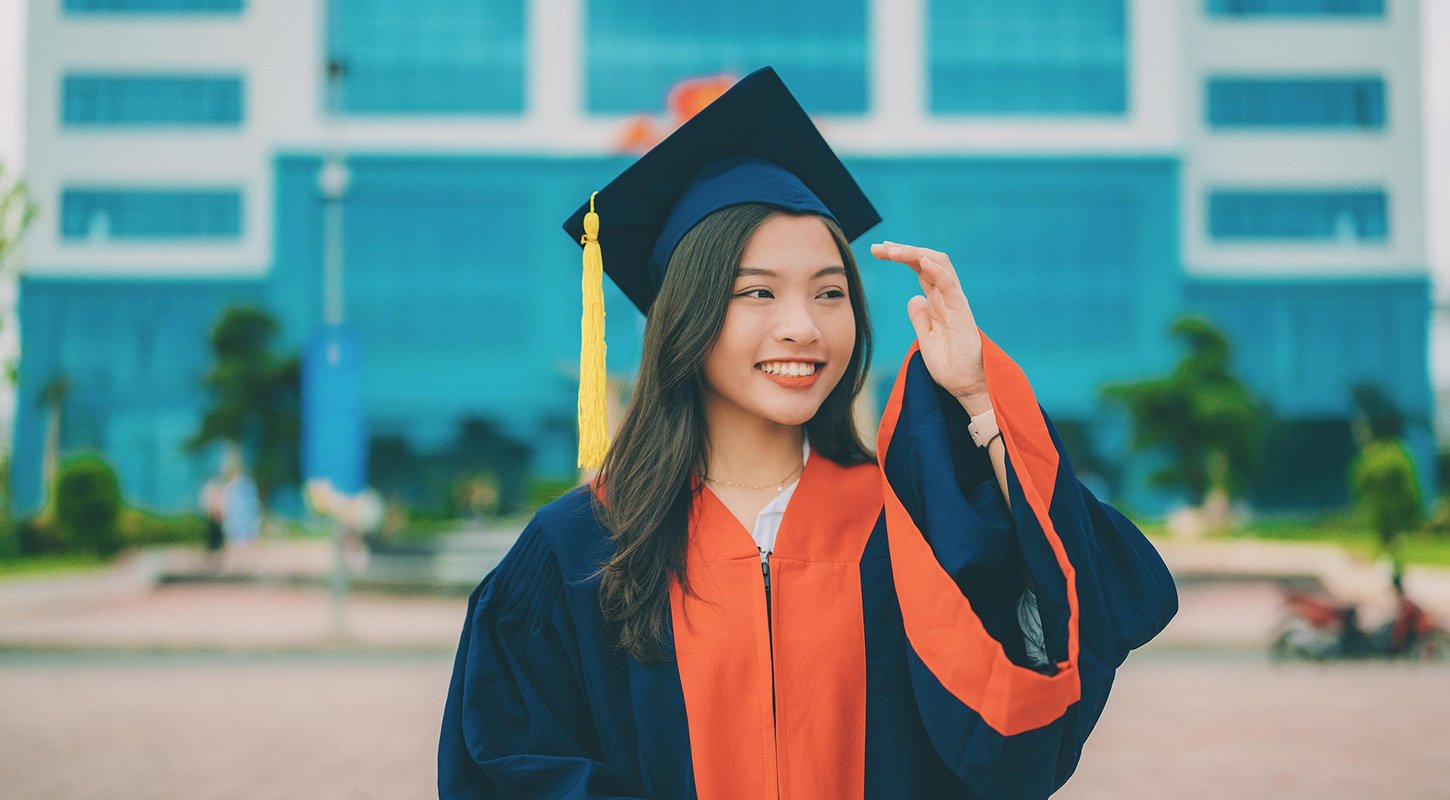 College graduate in cap and gown smiling on college grounds