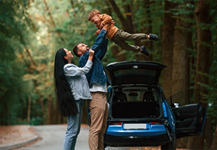 Smiling family of three on roadside while traveling with father holding son in the air