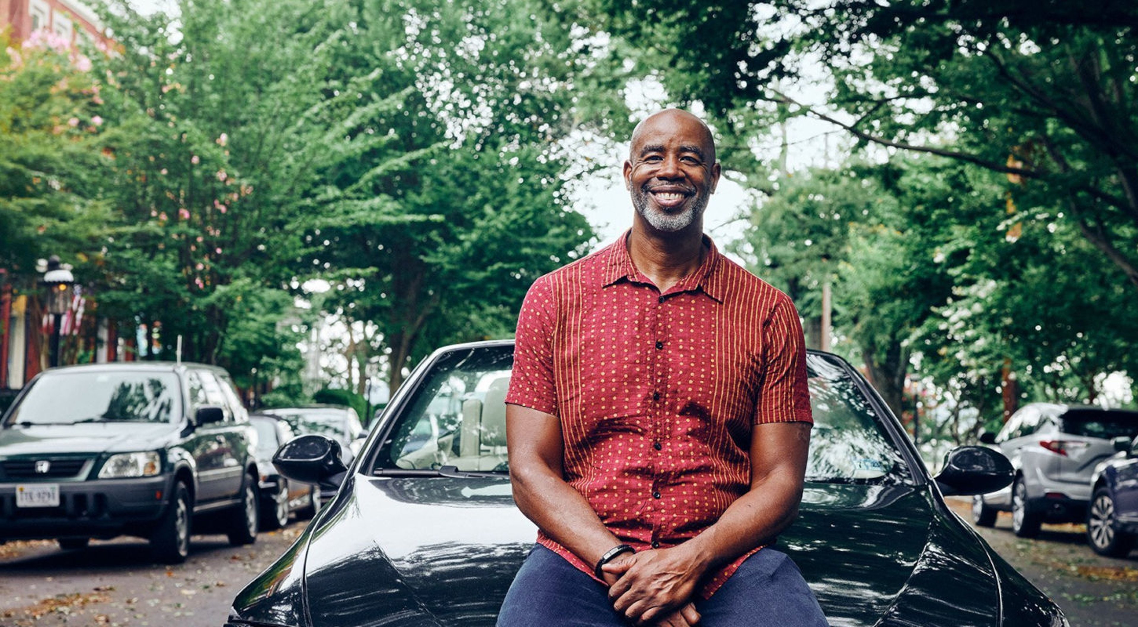 Smiling man sitting on car in red button down shirt