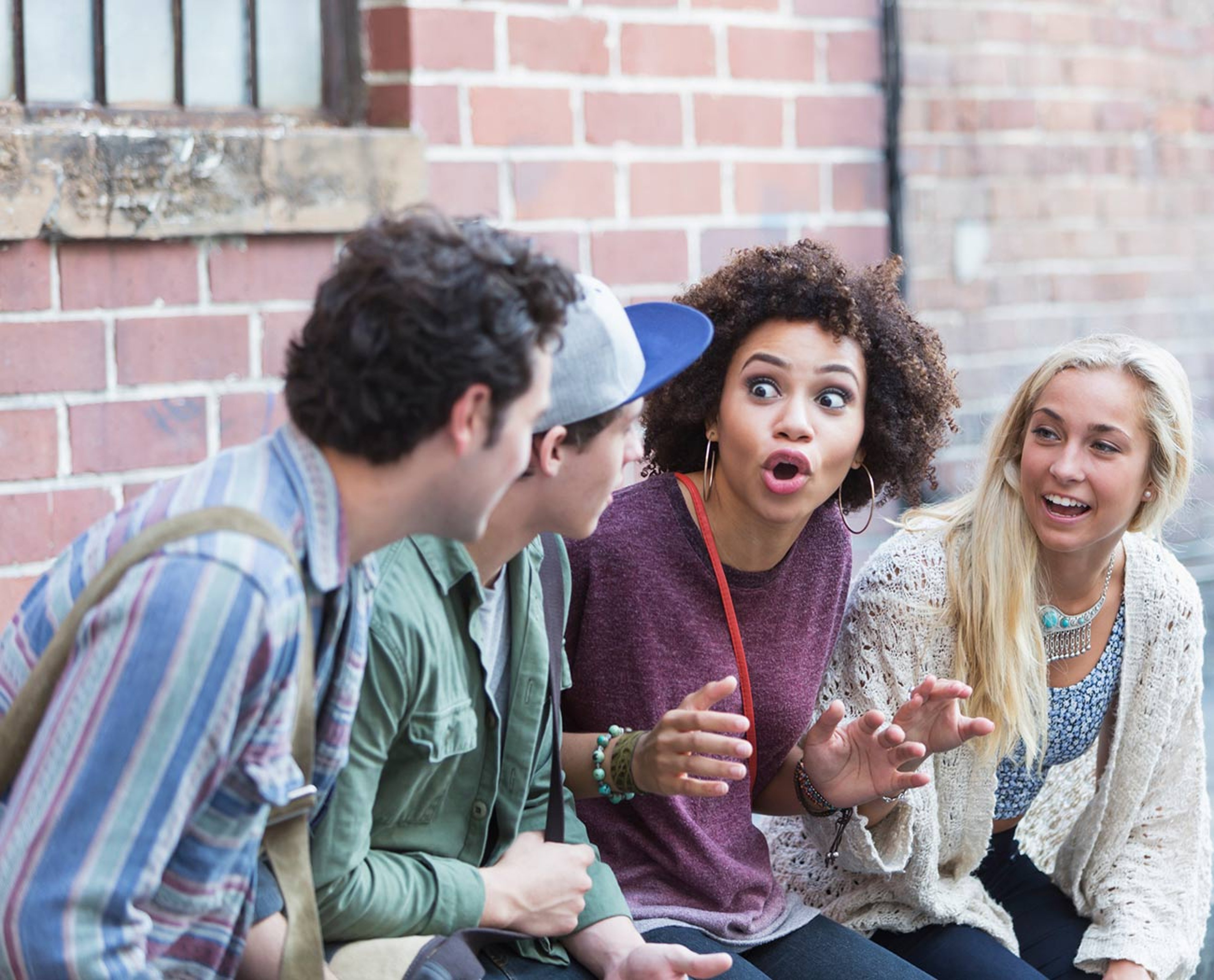 A group of four young adults talking animatedly in front of a brick wall.