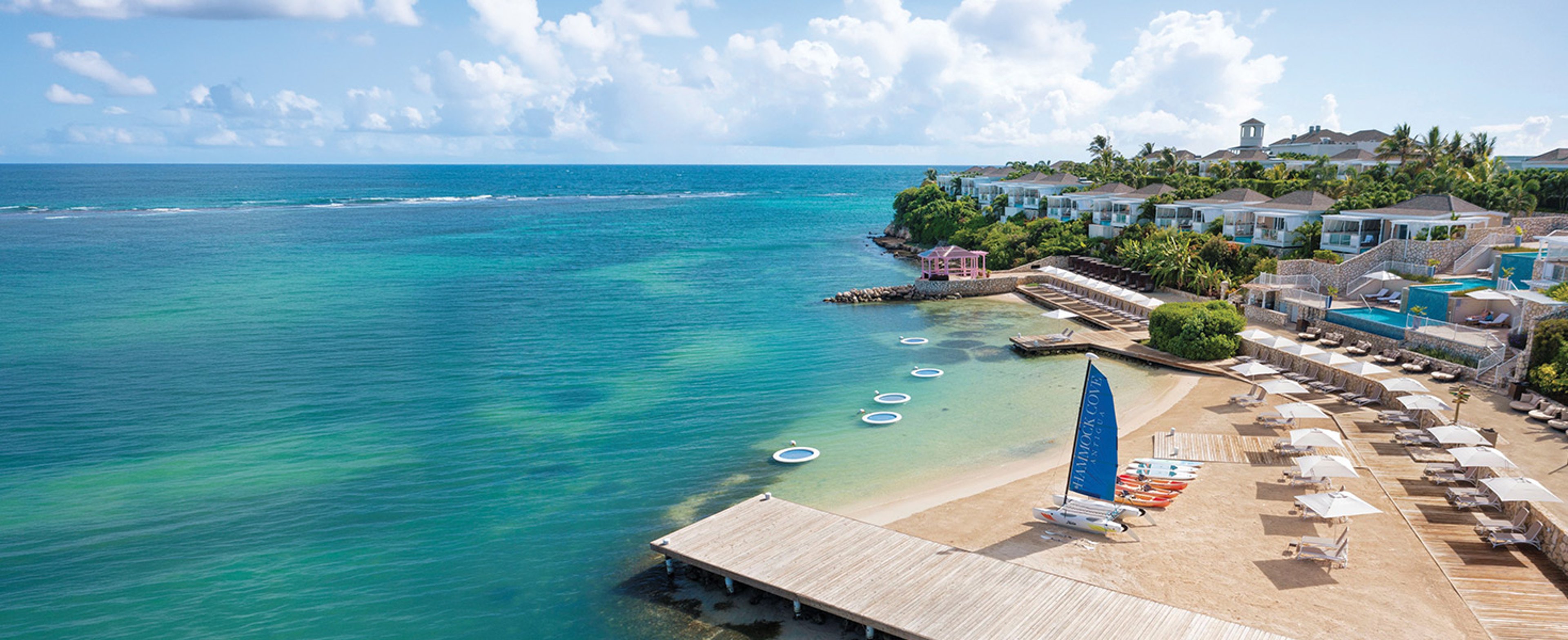 The image shows an aerial view of the waterfront and beach area at the luxury, adults-only Hammock Cove Antigua resort