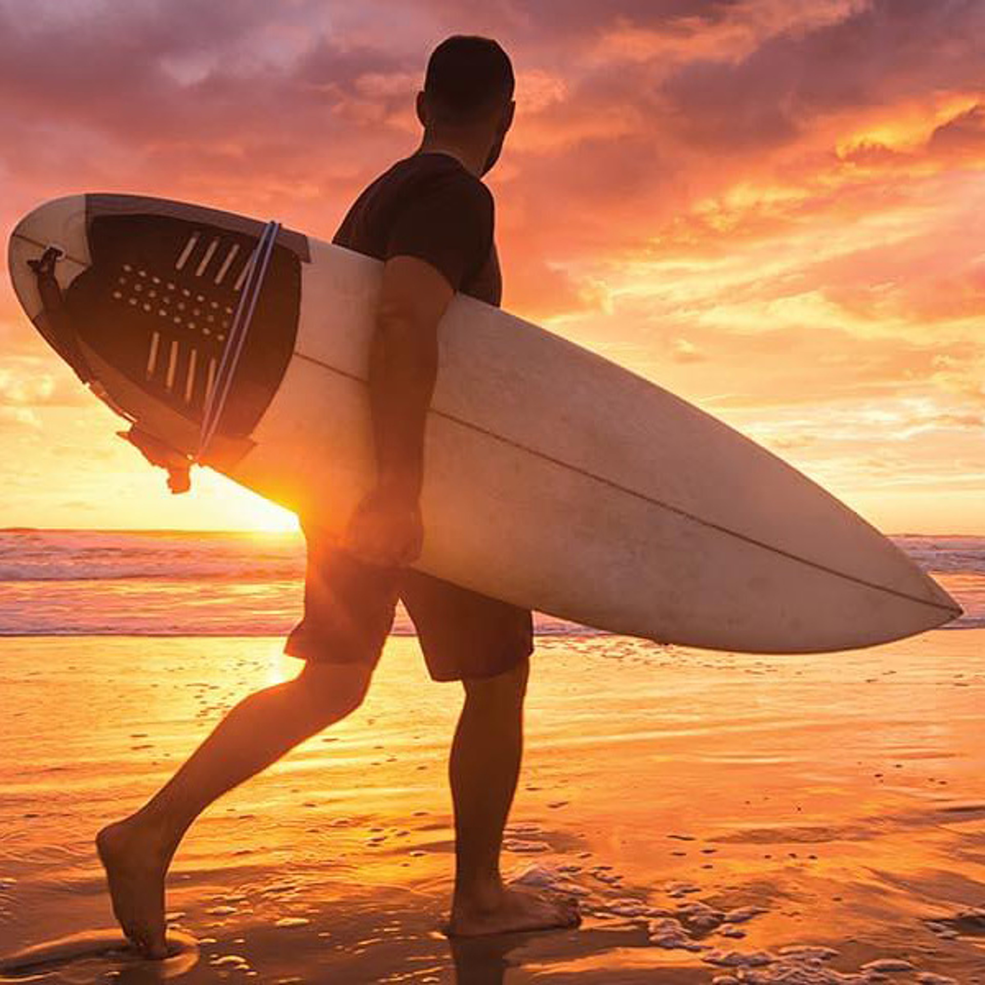 Silhouette of surfer carrying surfboard along the beach at sunset