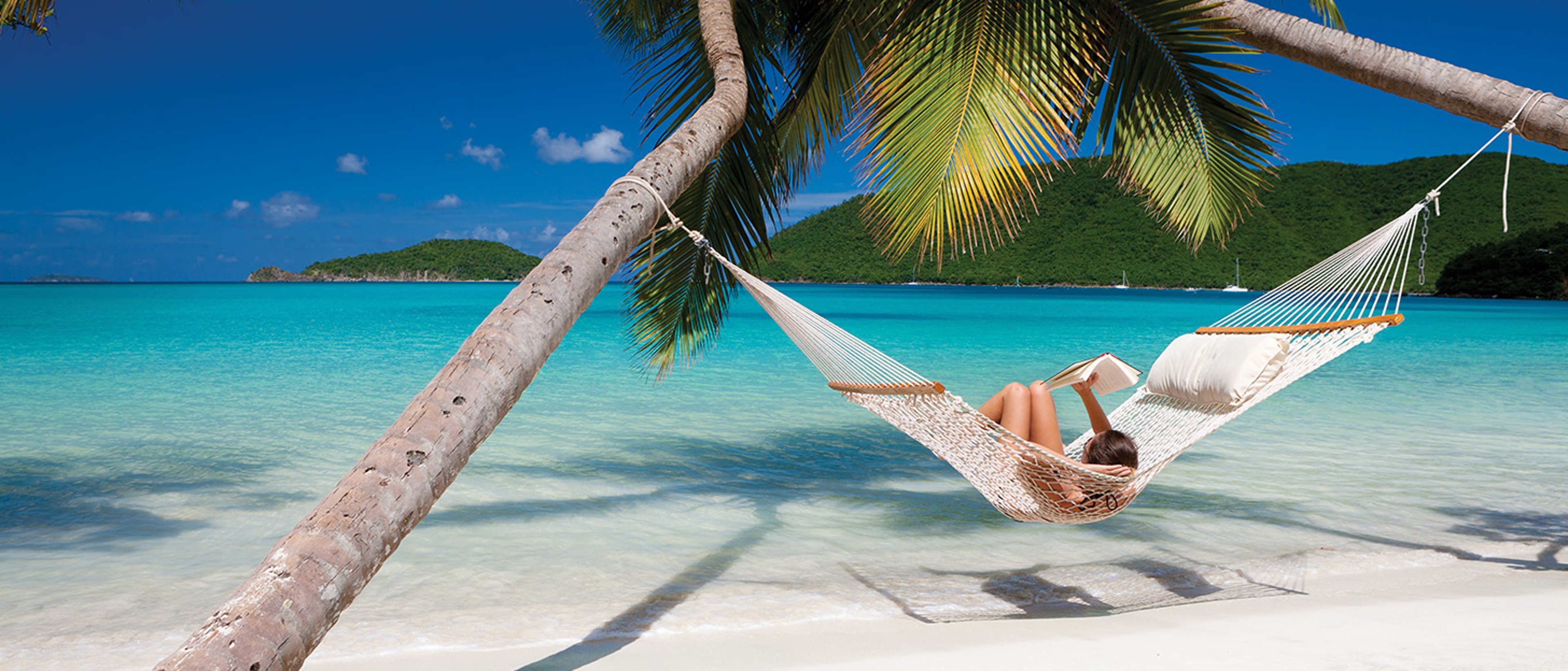 Woman reading in a hammock strung between two palm trees on a beautiful beach