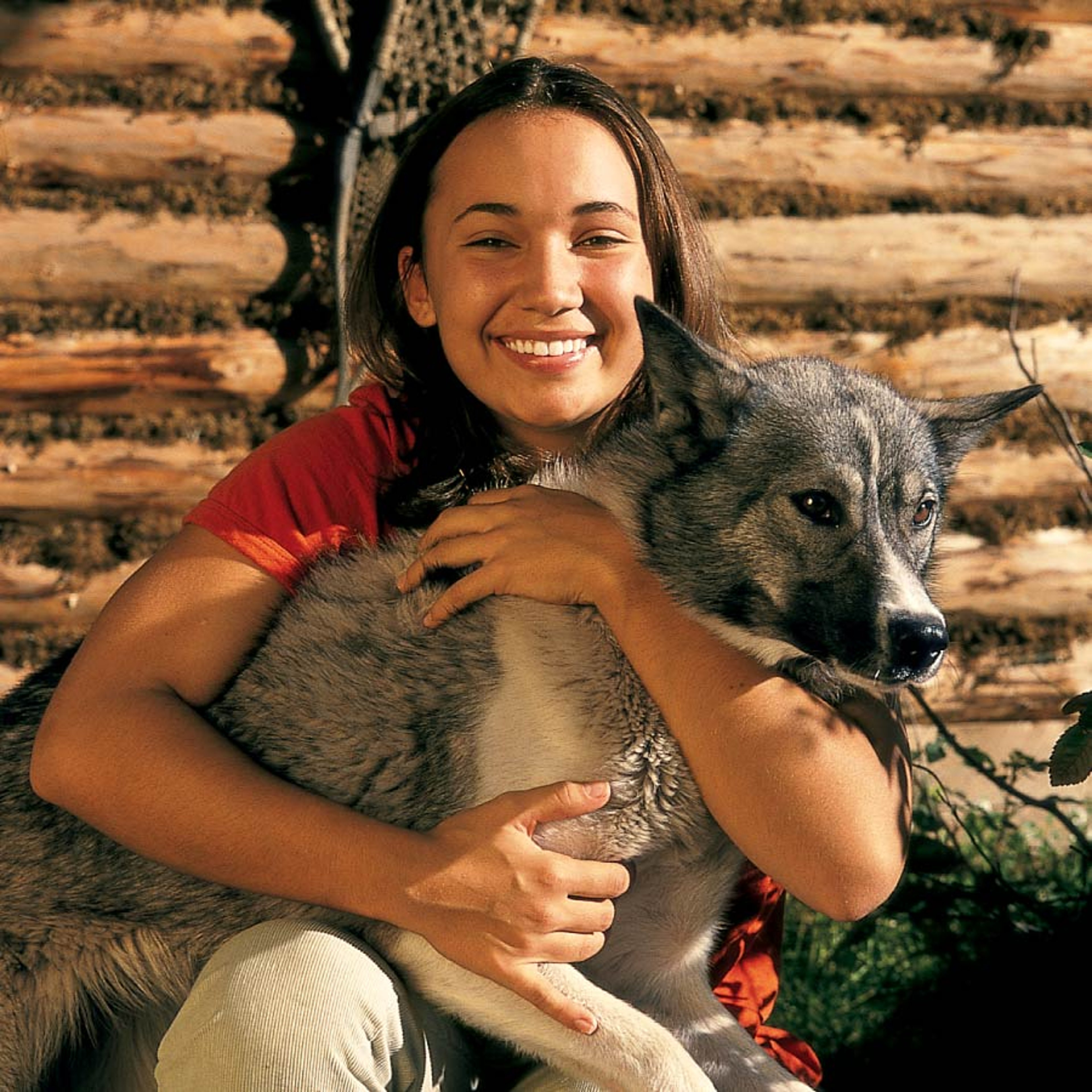 Woman holding a husky dog at a dog sled camp in Alaska, surrounded by sledding equipment