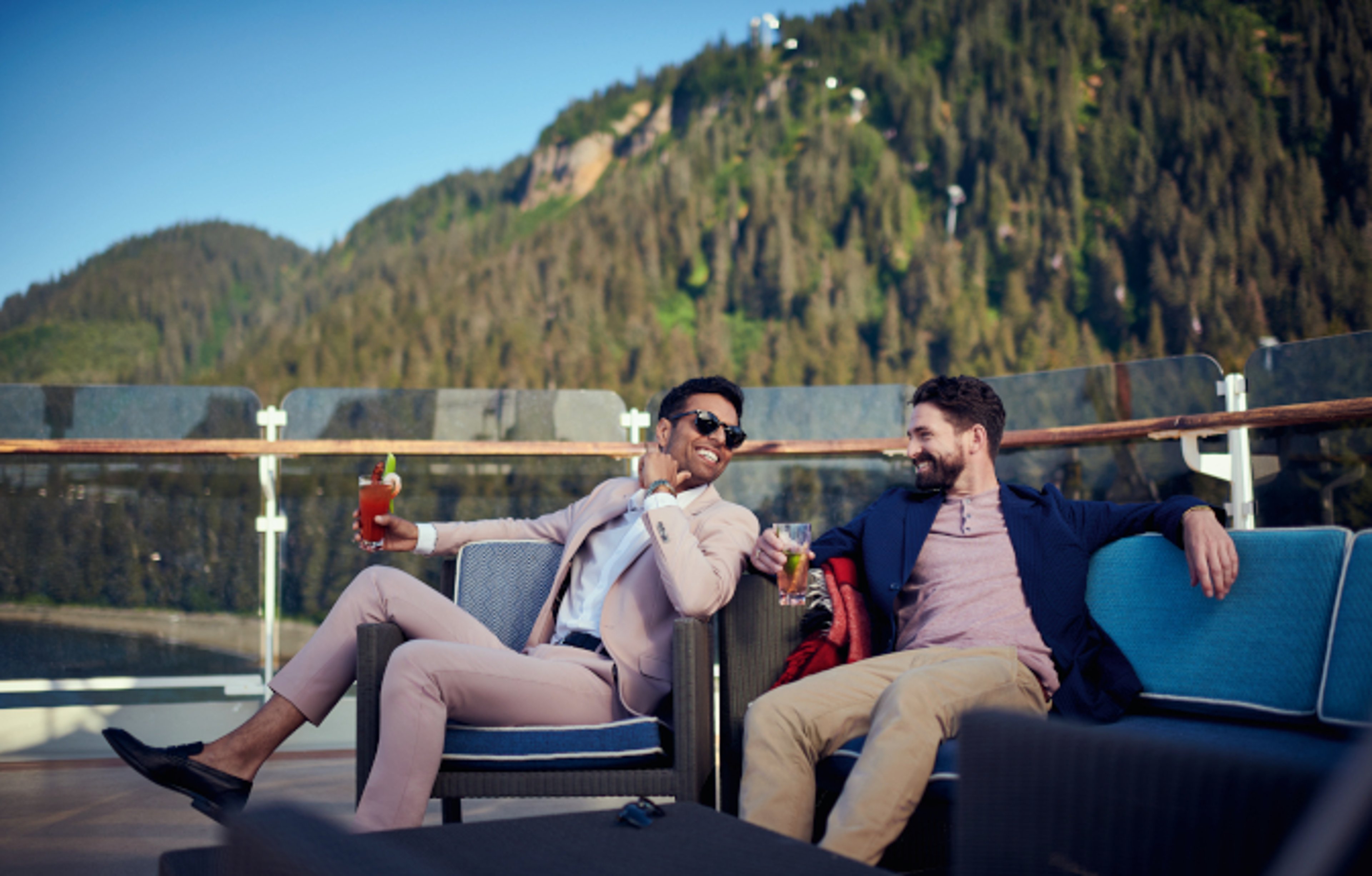 Men enjoying cocktails aboard the deck of Cunard ship with Alaskan mountains in background