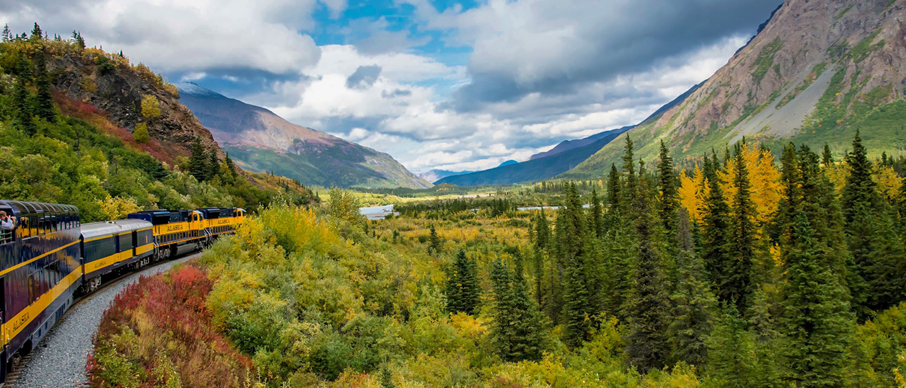 Alaska Railroad passenger train traveling through a mountainous landscape filled with autumn foliage