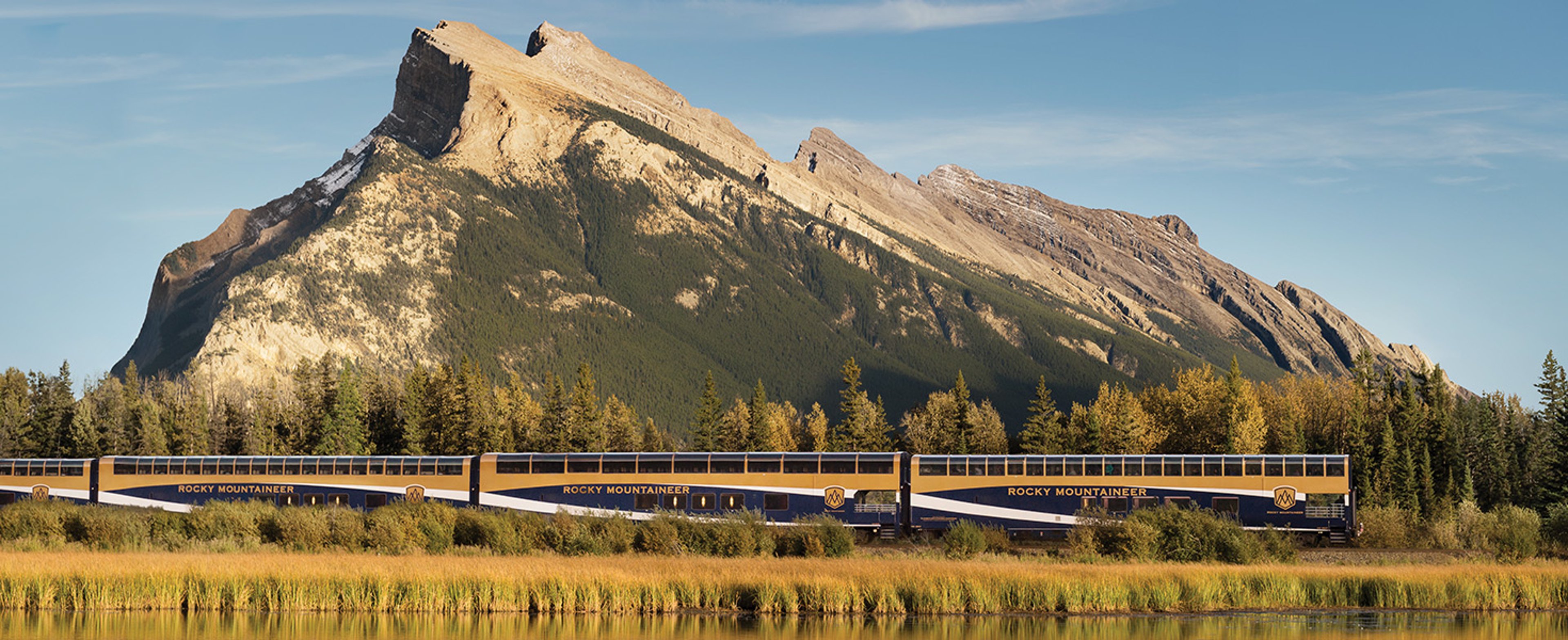 Rocky Mountaineer train traveling through the Canadian Rockies right past Mount Rundle.