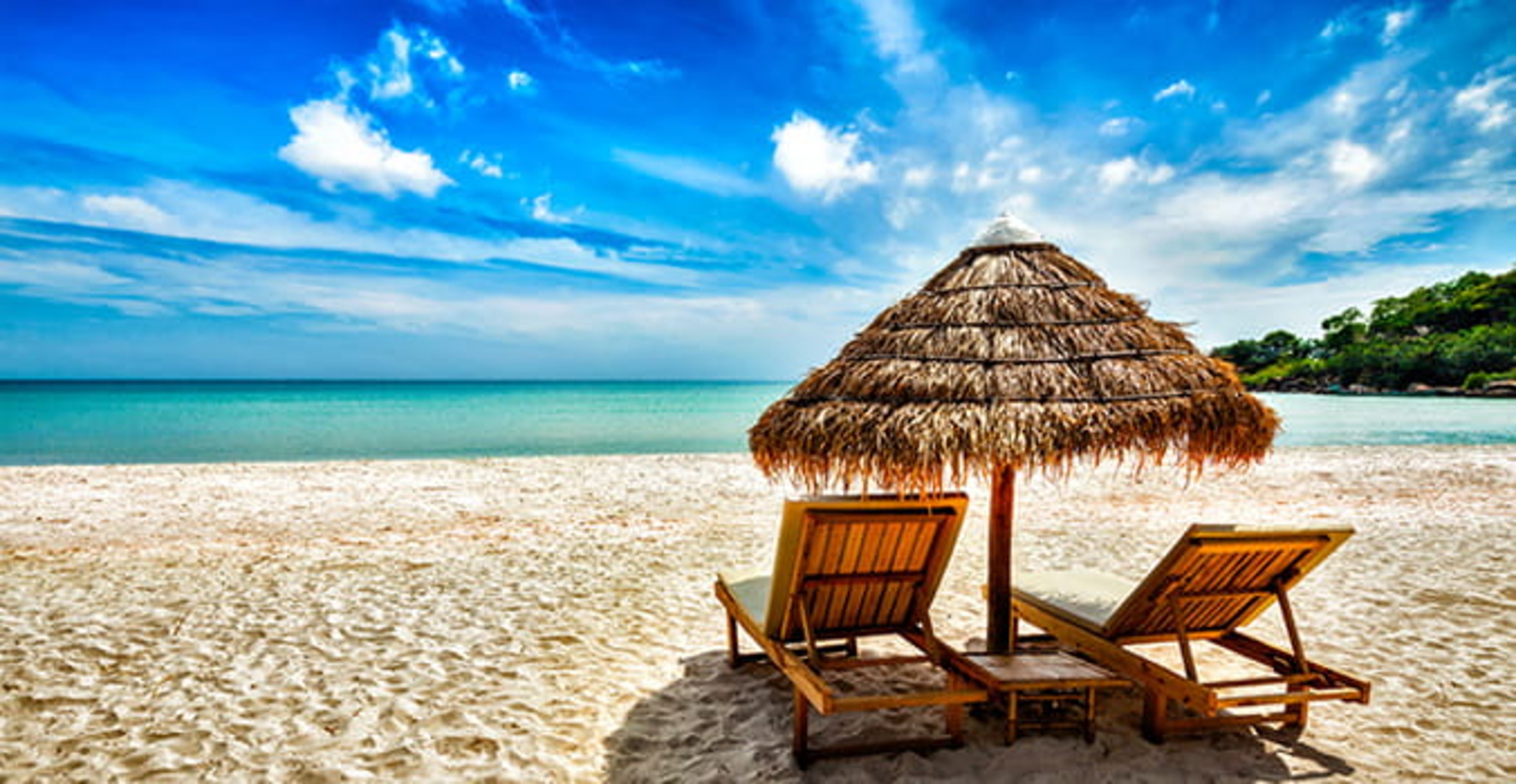 Thatch umbrella next to two chairs on a sandy beach